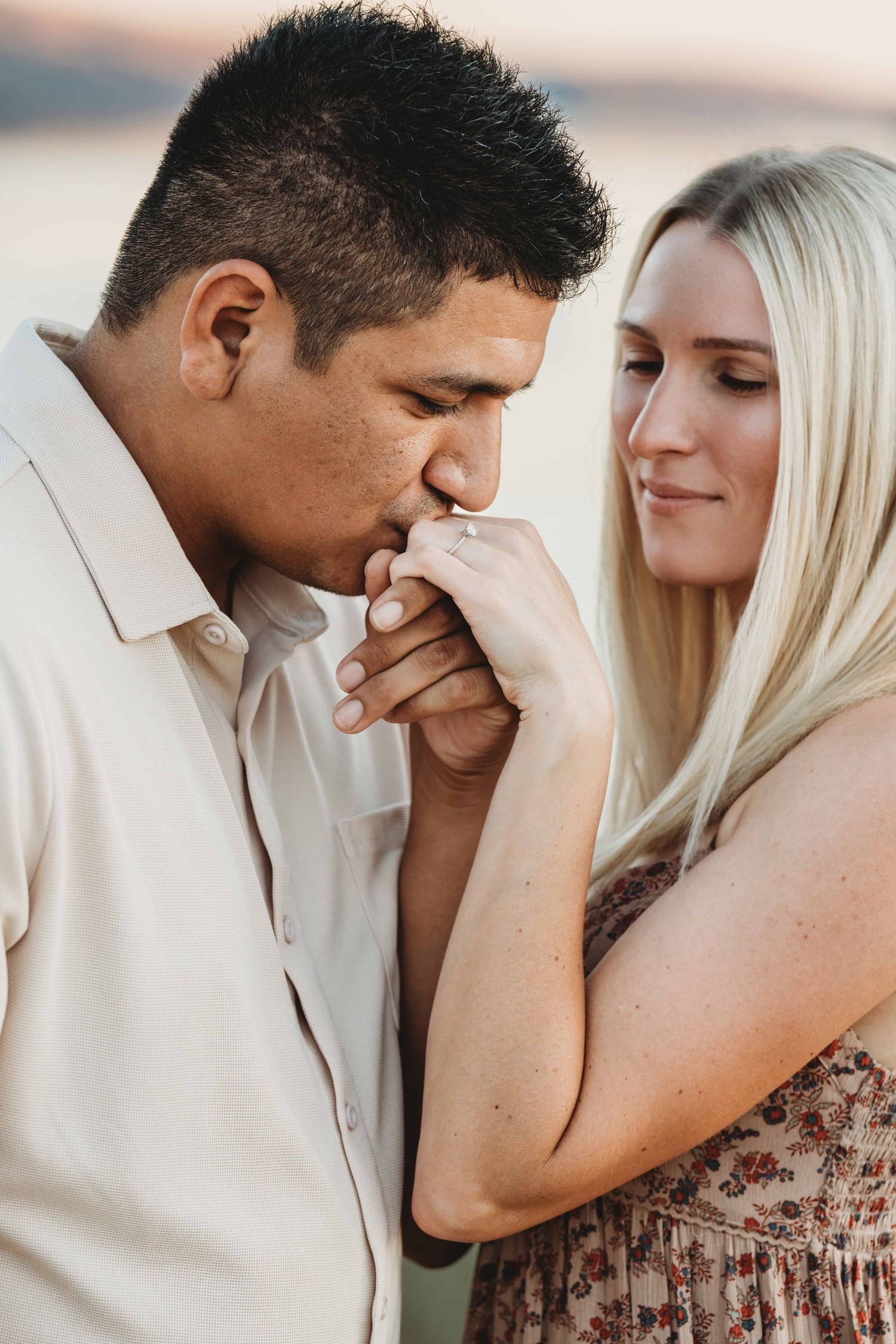 A man kissing his fiancés hand while she looks at him with a content look on her face.