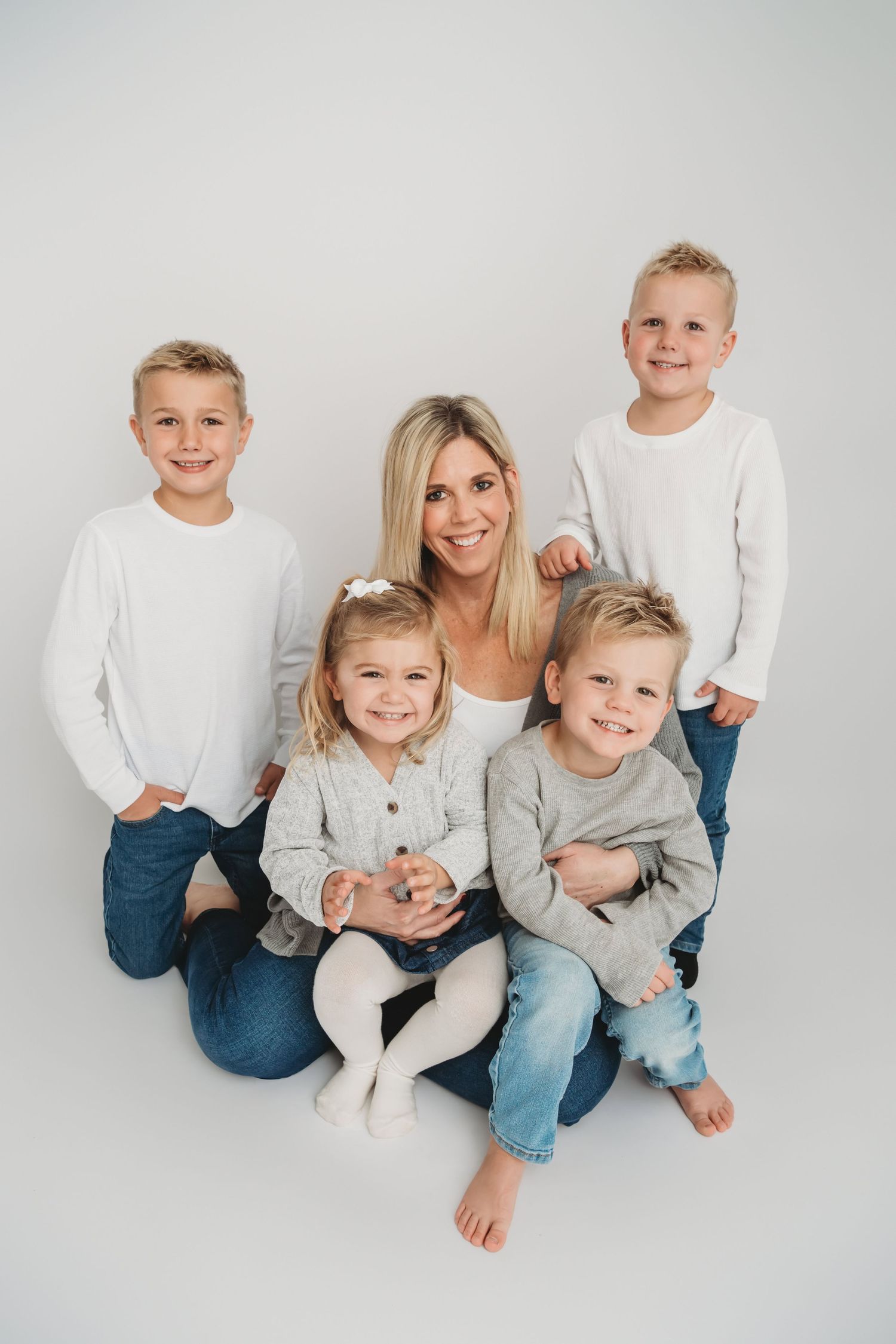 A mom and her four children smiling for a portrait on a white studio backdrop.