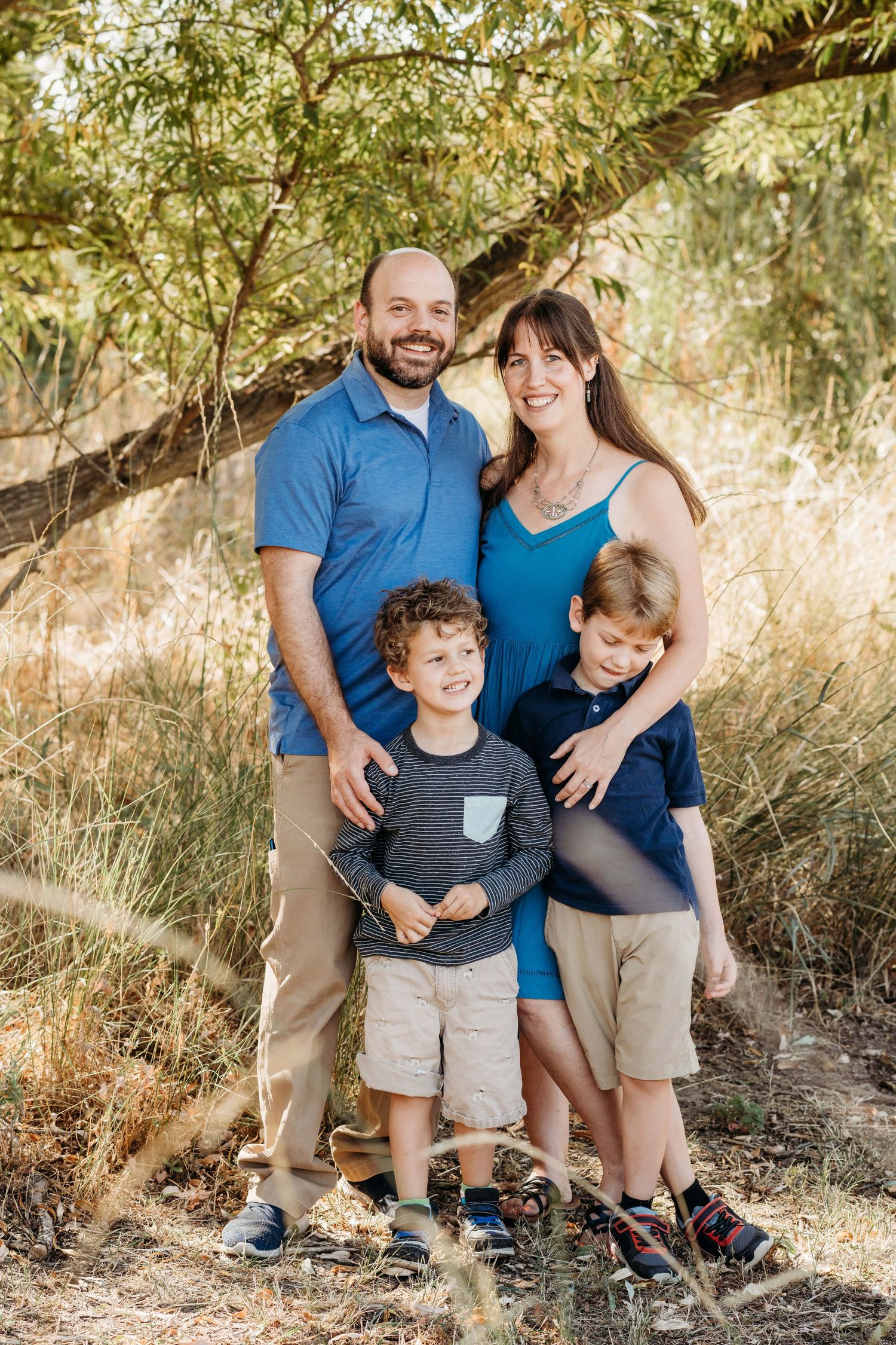 Outdoor family photography in Walla Walla featuring parents and two children standing together beneath trees.