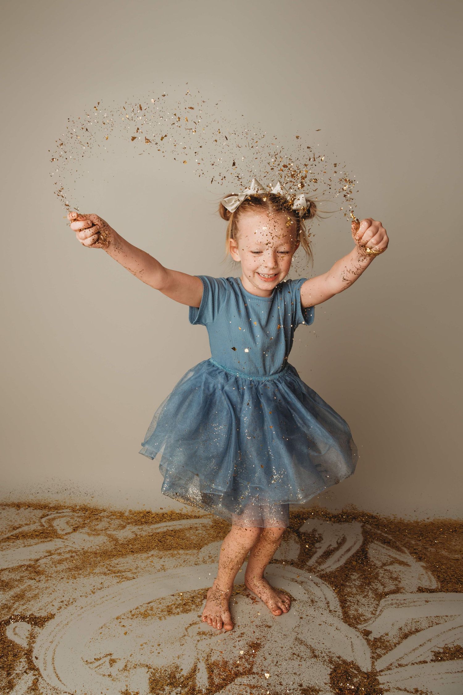 A little girl wearing a blue dress dances while throwing glitter in the air.