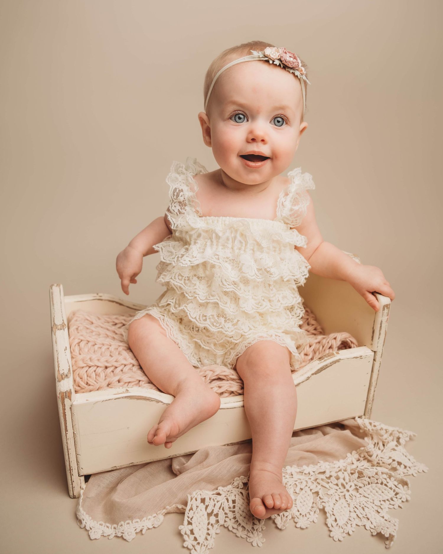A baby girl sitting in a vintage style wooden bed smiling.