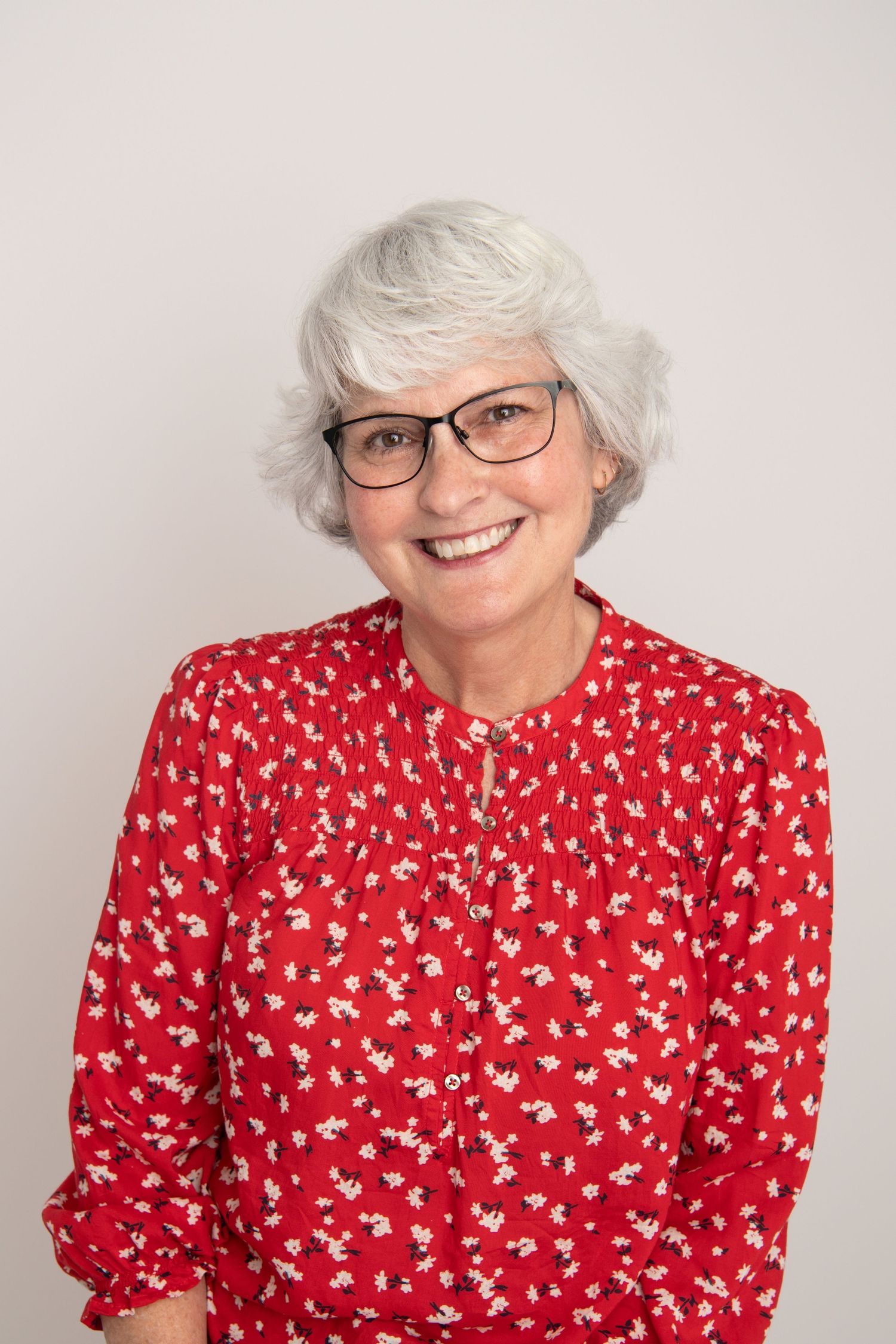 A headshot portrait of a woman with glasses wearing a red shirt.