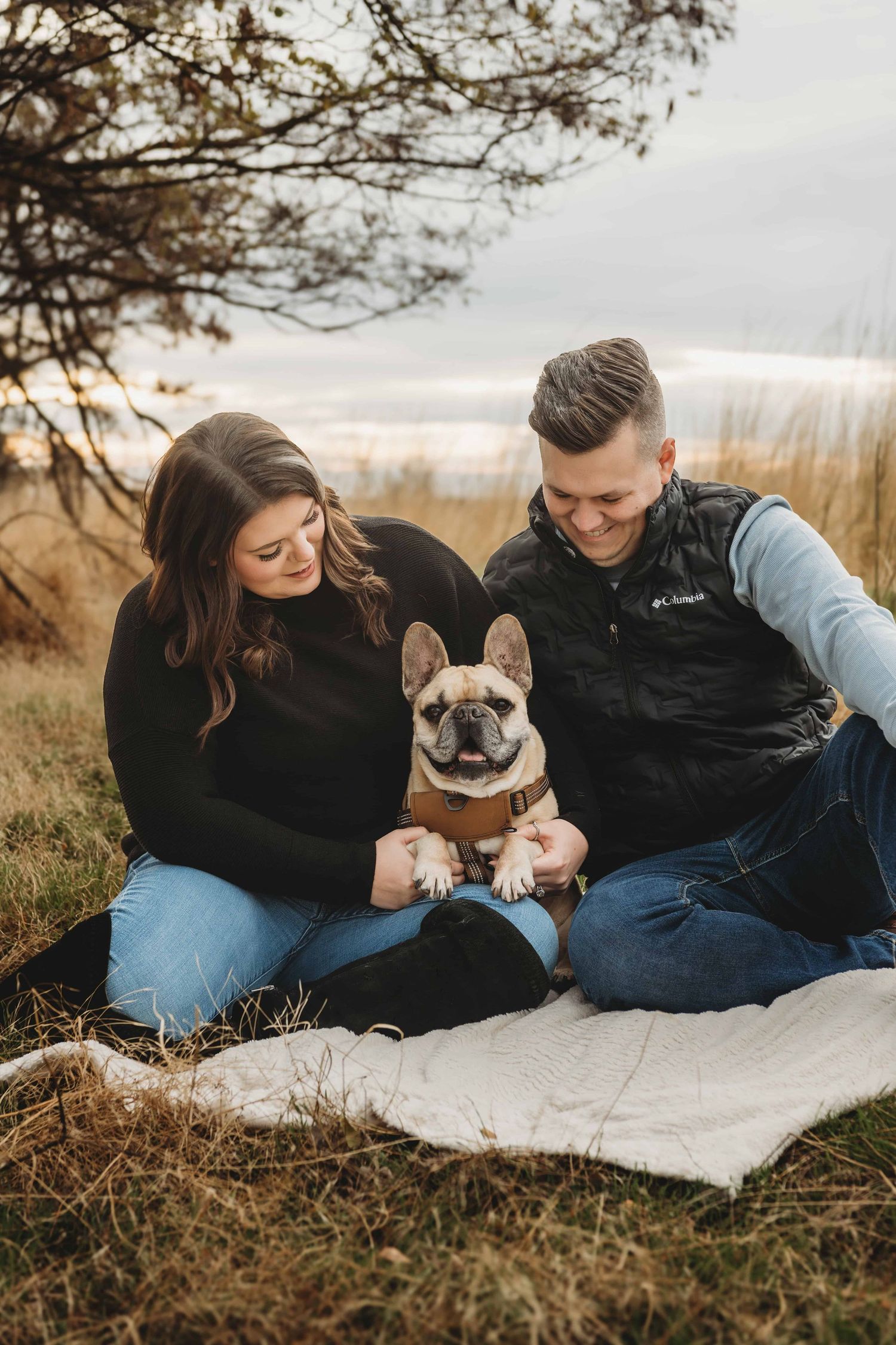 A couple and their dog sitting on a blanket underneath a tree in Walla Walla.