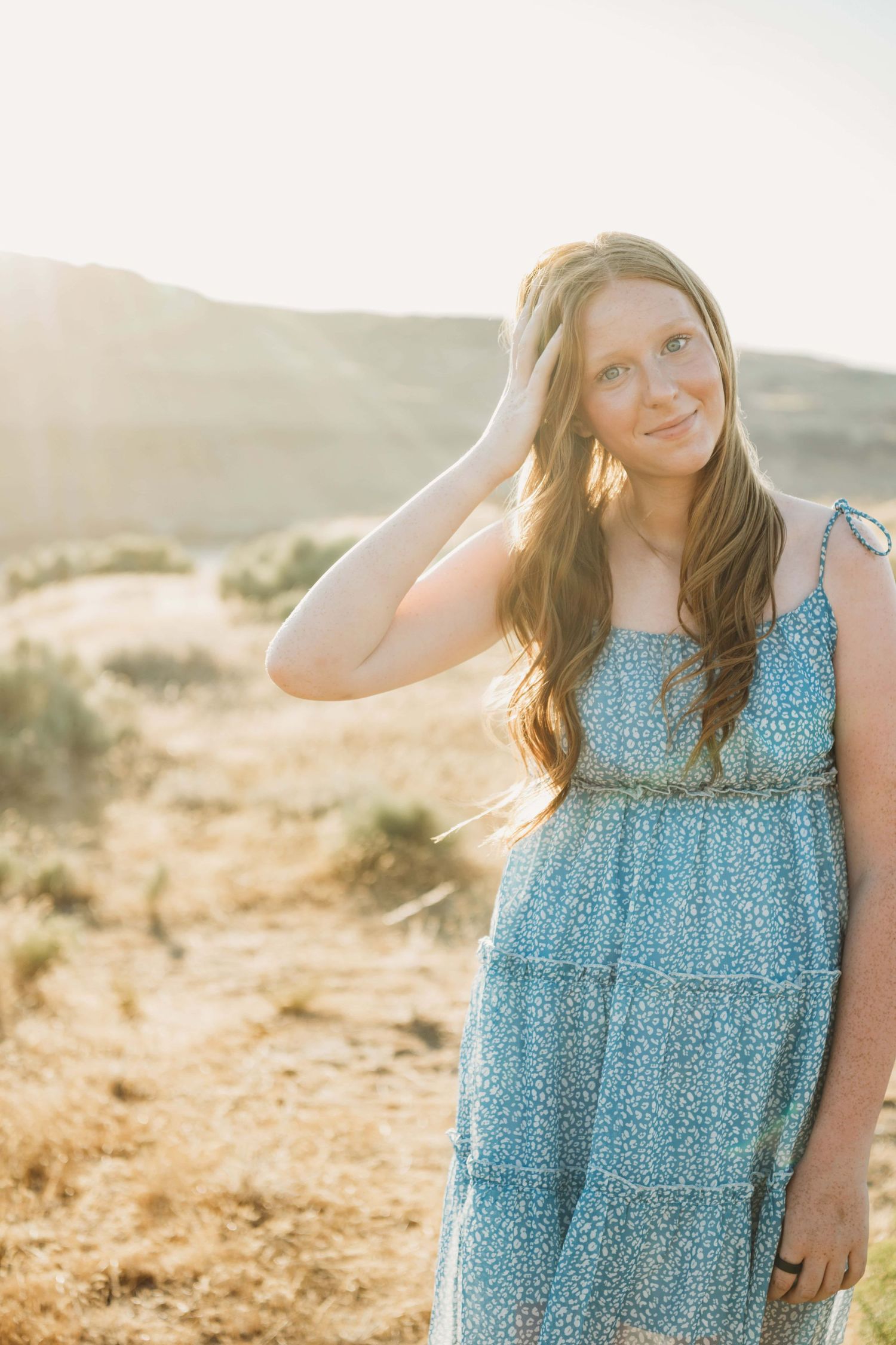 A young woman in a blue dress running her hand through her hair during a golden hour senior session in Walla Walla.