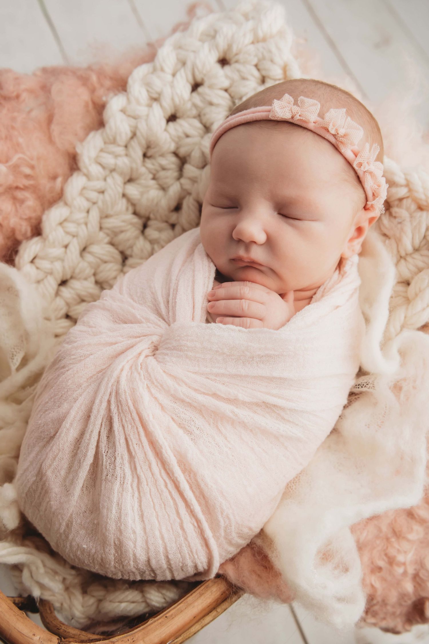 A newborn baby girl wrapped in soft pink sleeping in a boho bassinet.