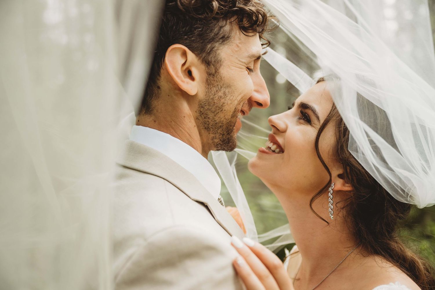 A bride smiling at her groom while underneath her veil.