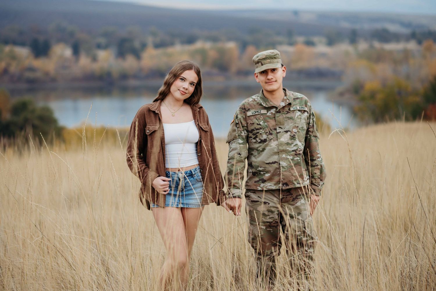A couple looking at the camera with a lake in the background.