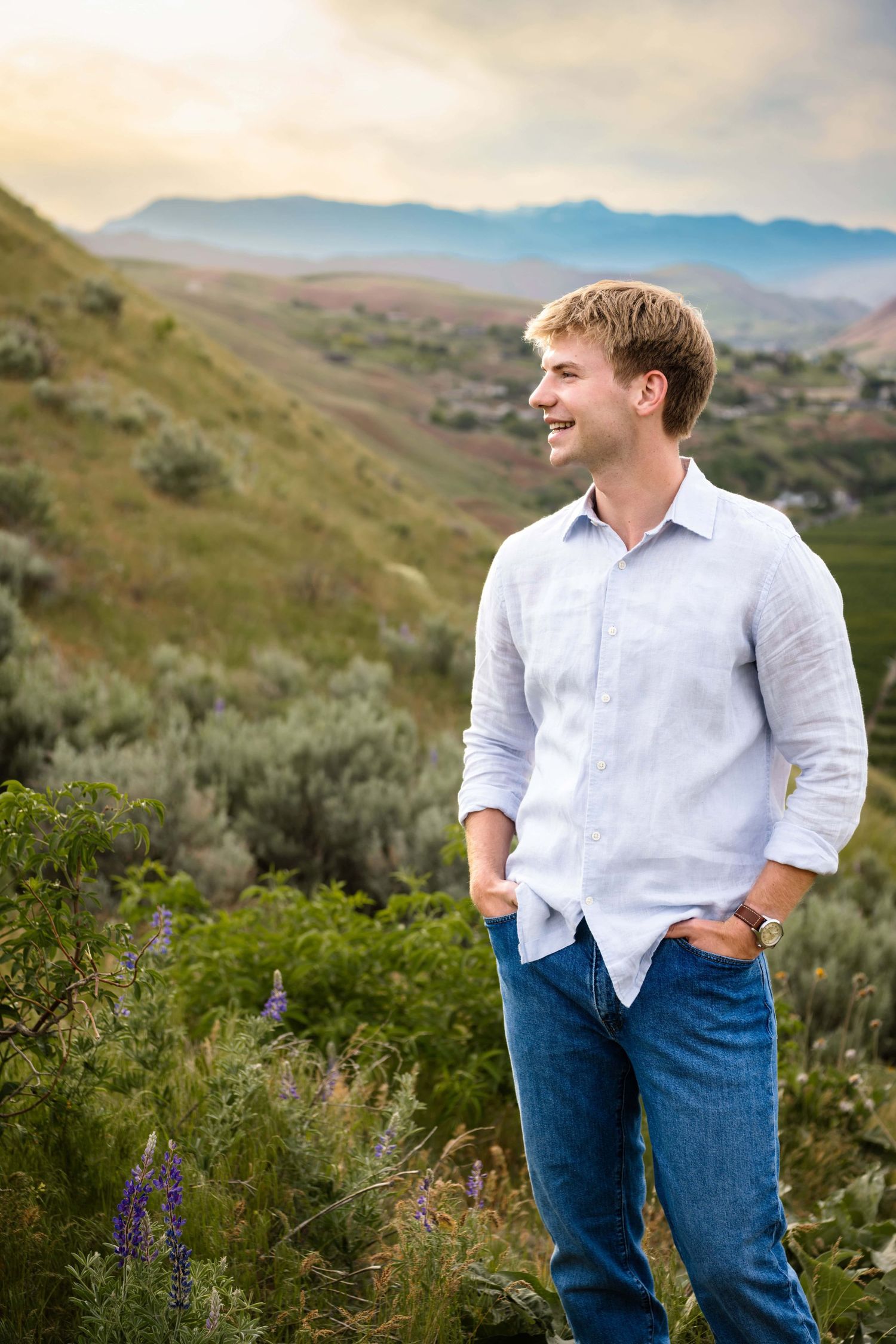 A man with colorful landscape and mountains in the background, looking off into the distance smiling.
