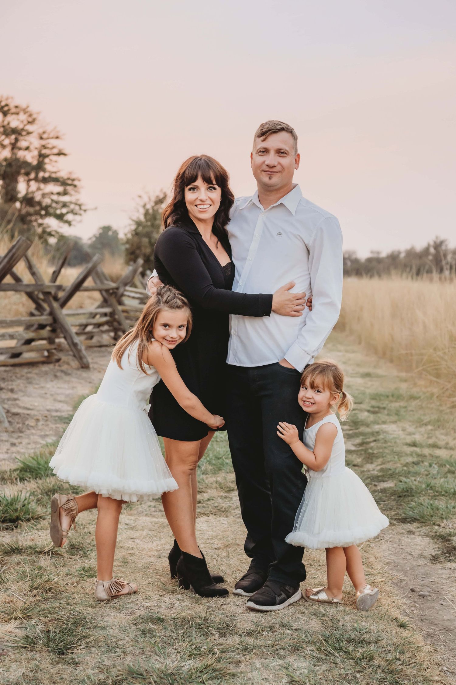 Family portrait by a Walla Walla photographer featuring parents and children standing together at sunset near a rustic fence.