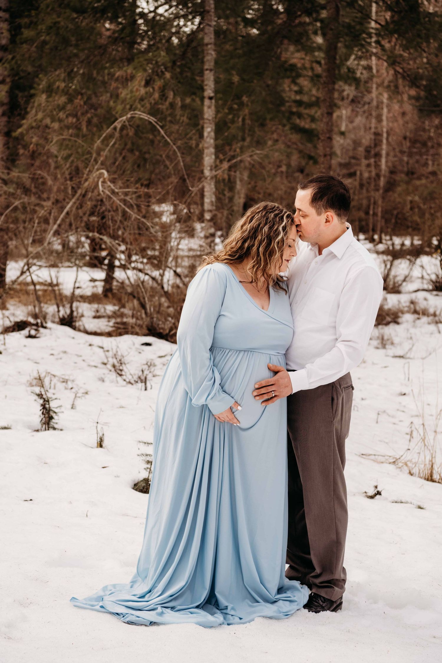 An expecting couple embraces each other while standing in snow in Walla Walla, Washington.