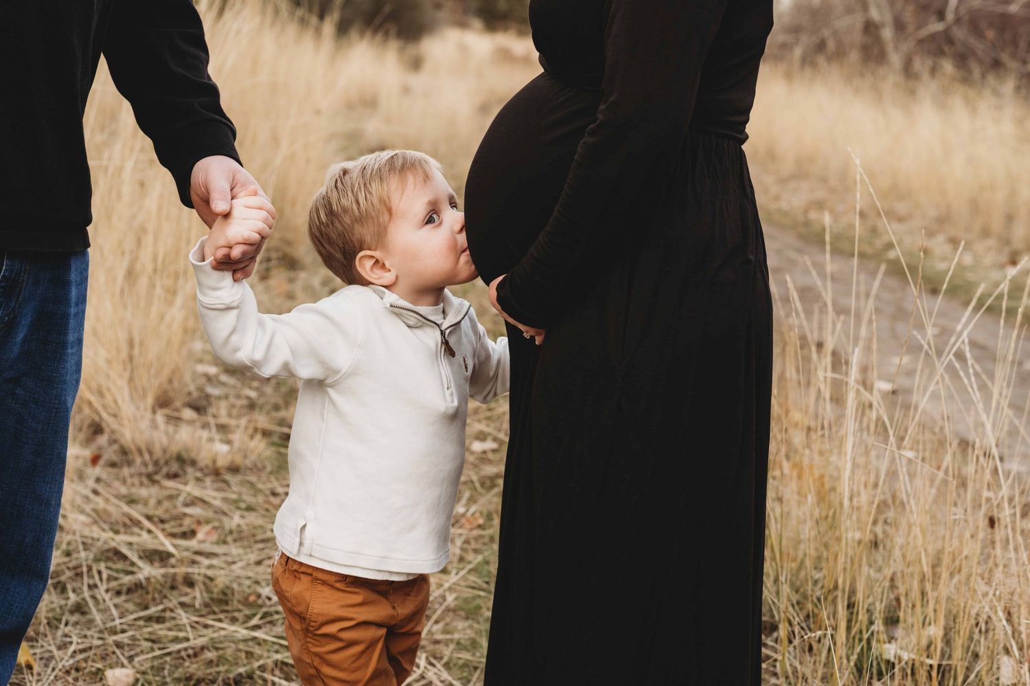 Family maternity photography in Walla Walla showing a young child kissing a pregnant belly during an outdoor session.