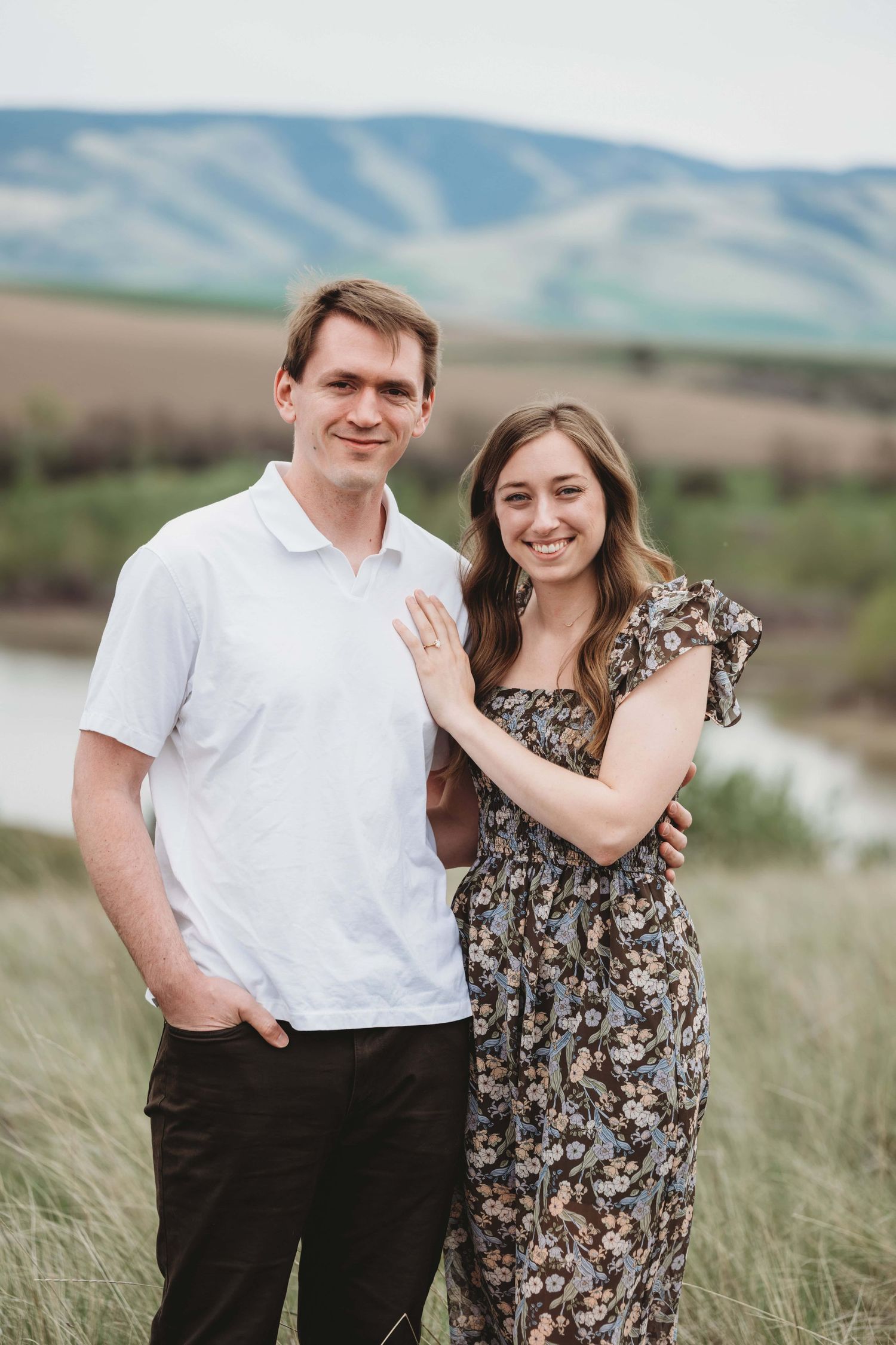 A man and woman looking at the camera, smiling with blue rolling hills in the background.