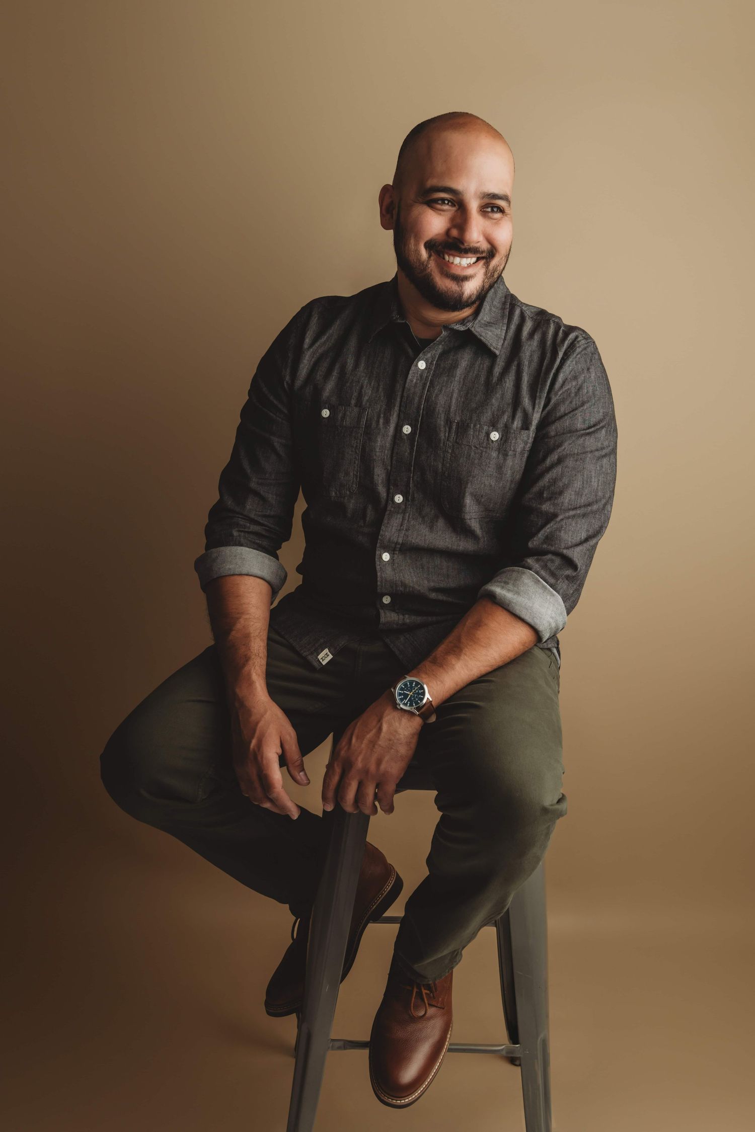 A portrait of a man sitting on a tall stool on a brown backdrop in a Walla Walla photography studio.
