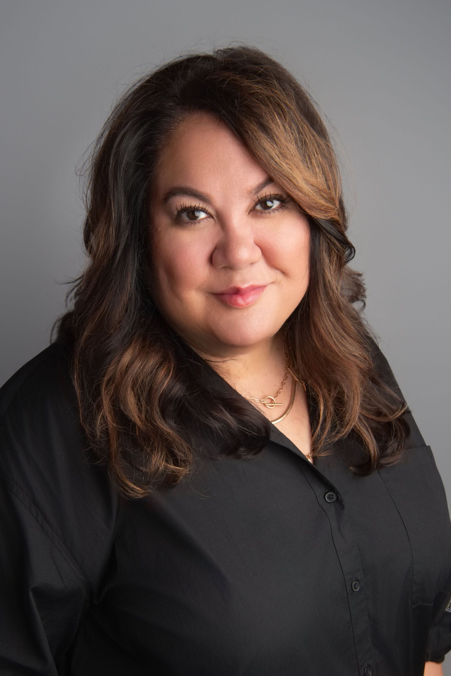 A professional headshot of a woman wearing a black shirt on a gray backdrop.