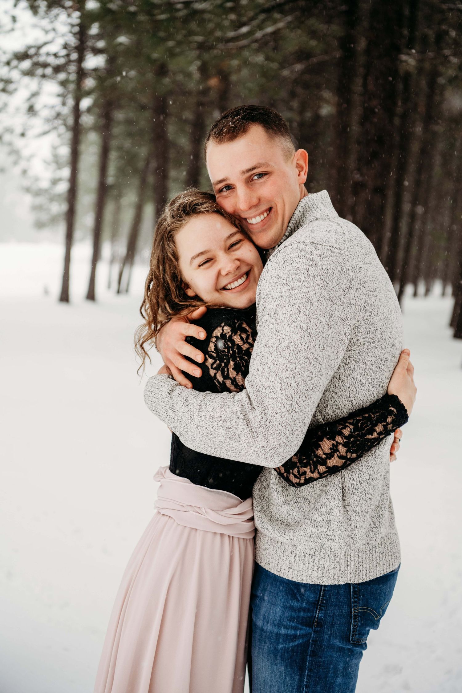 Couples portrait by a Walla Walla photographer capturing an engaged couple embracing in a snowy forest setting.