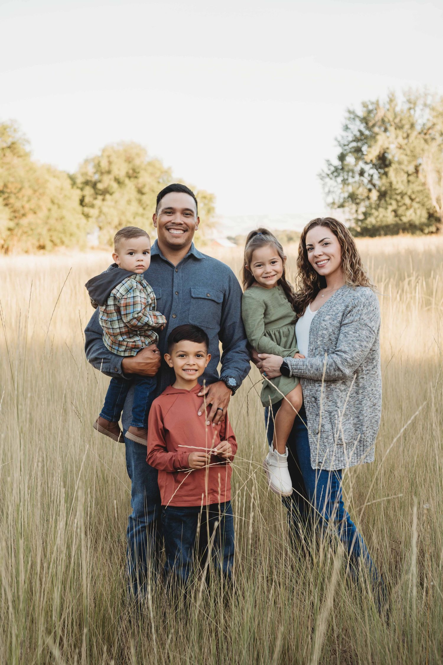 A family of five standing in an open field and smiling for the camera.