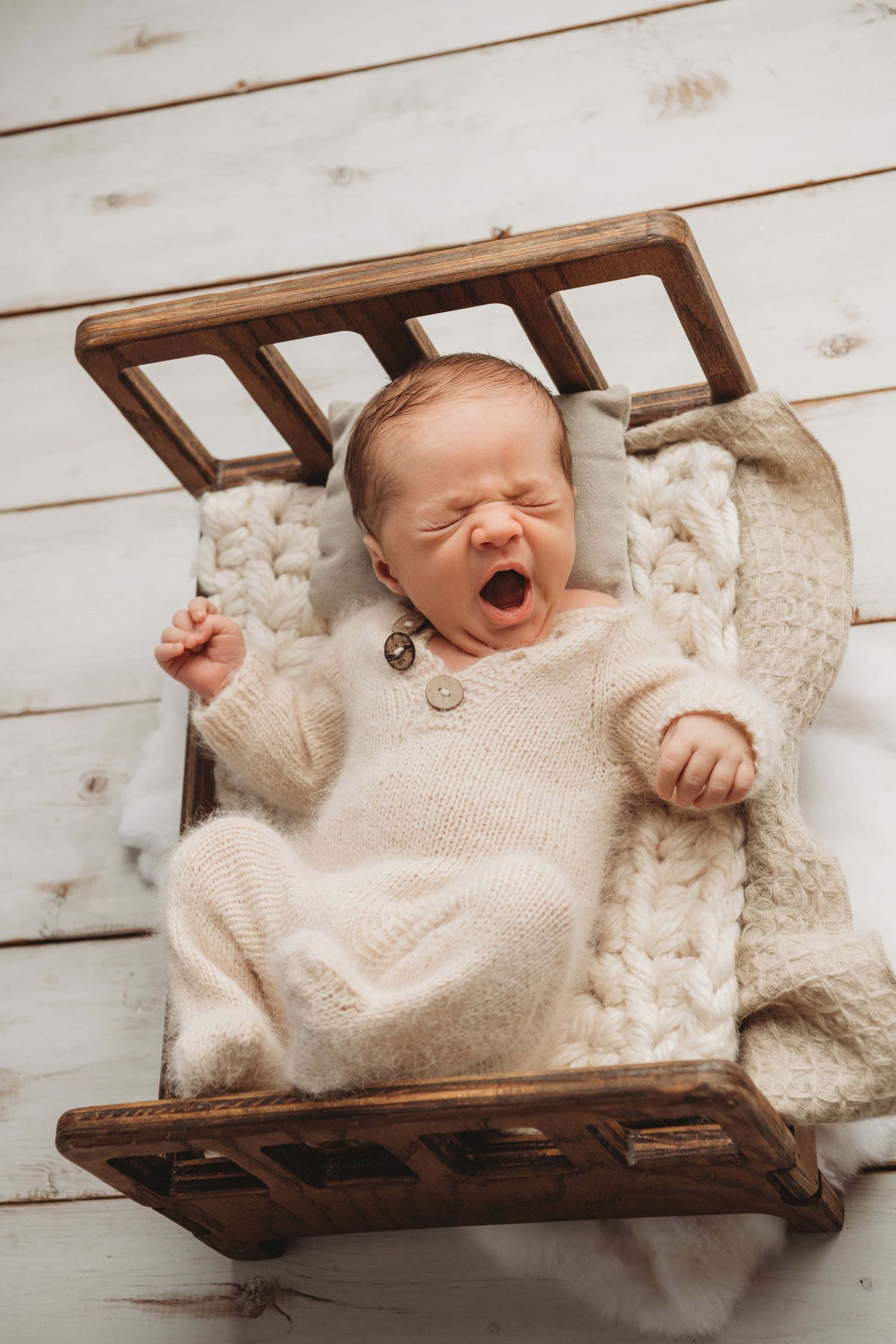 A sleepping baby yawning on a brown wooden bed surrounded by neutral tones.