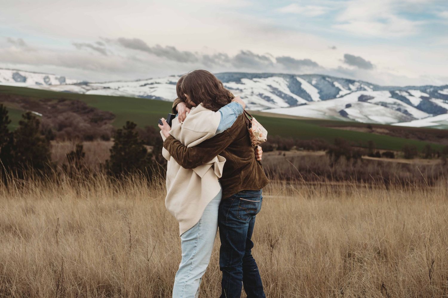 A couple embracing just after getting engaged with snow covered mountains in the background.