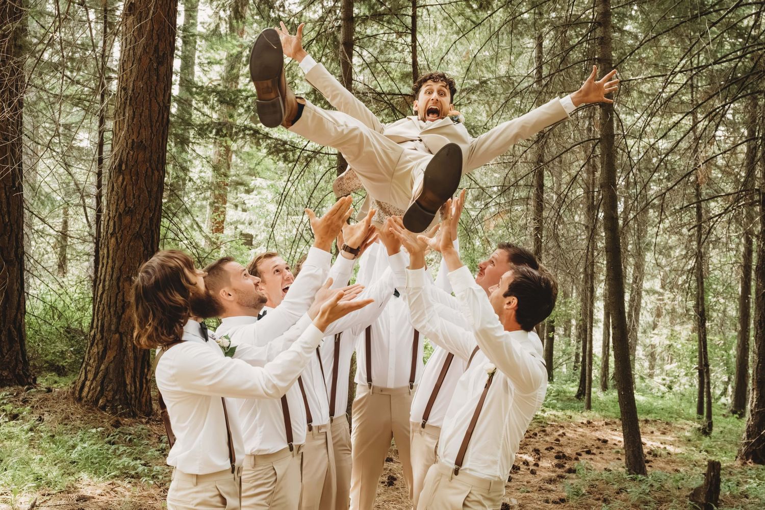 A group of groomsmen throwing the groom in the air as he makes a surprised expression.