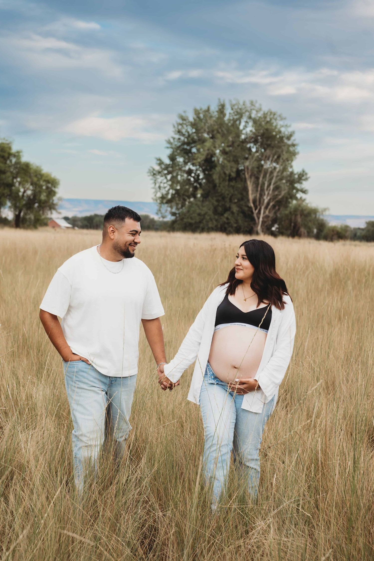 An expecting couple walks through a field during sunset in Walla Walla, Washington.