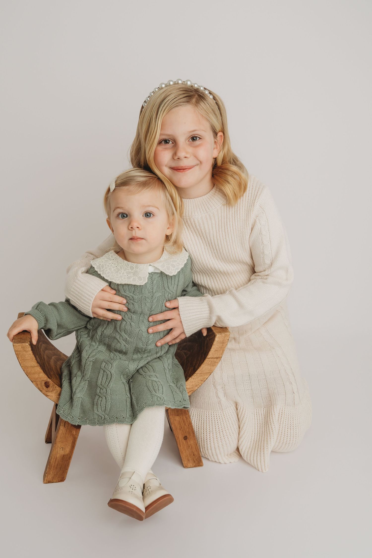 A timeless portrait of two sisters on a wooden stool dressed in green and cream.