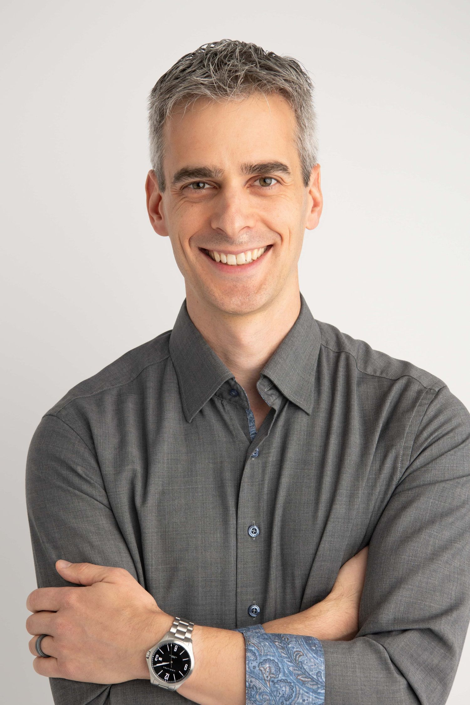 A professional headshot of a man with his arms crossed wearing a watch.