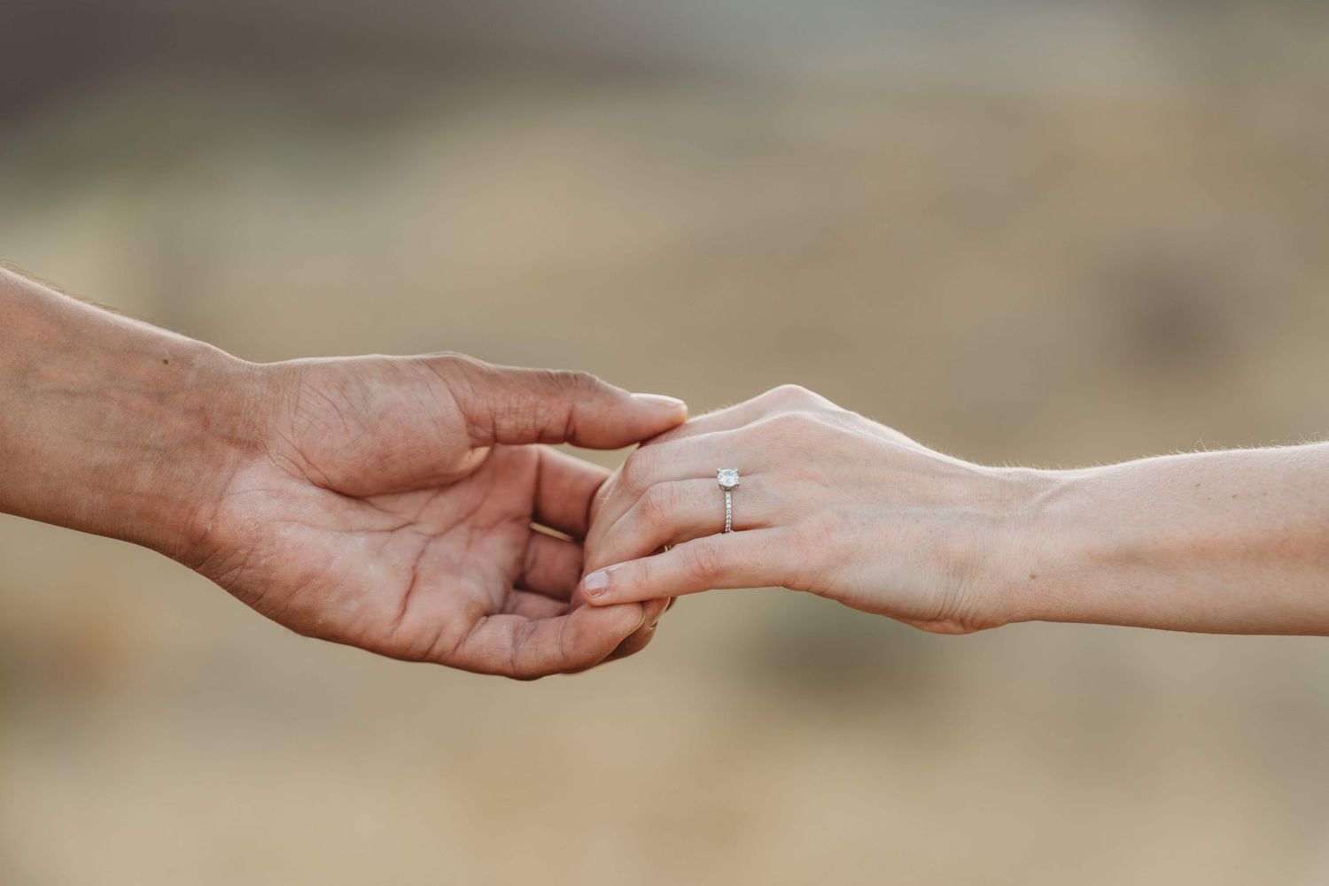 A detail shot of a man and woman holding hands showing off her engagement ring.