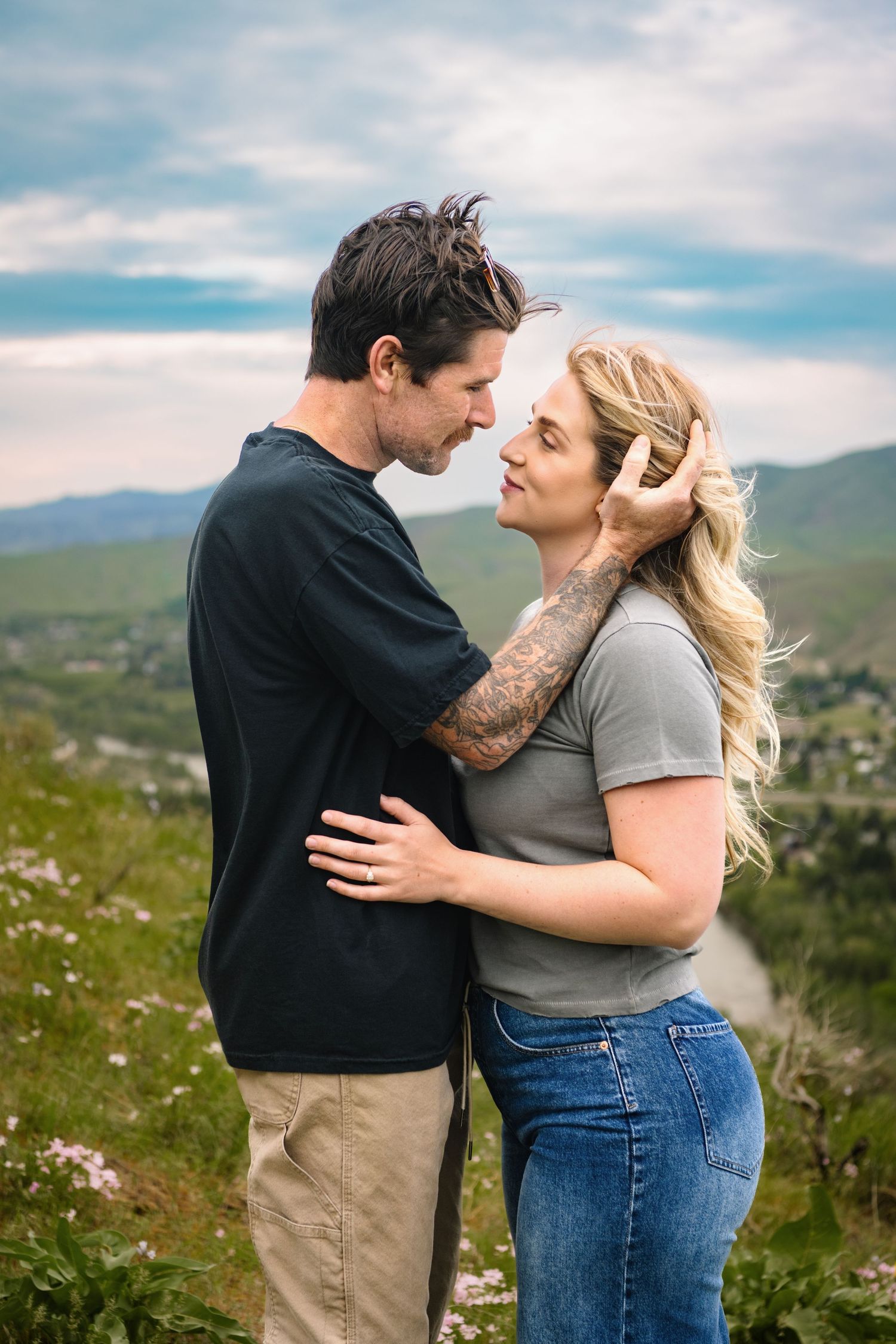 A couple embracing with green mountains and a dramatic sky.