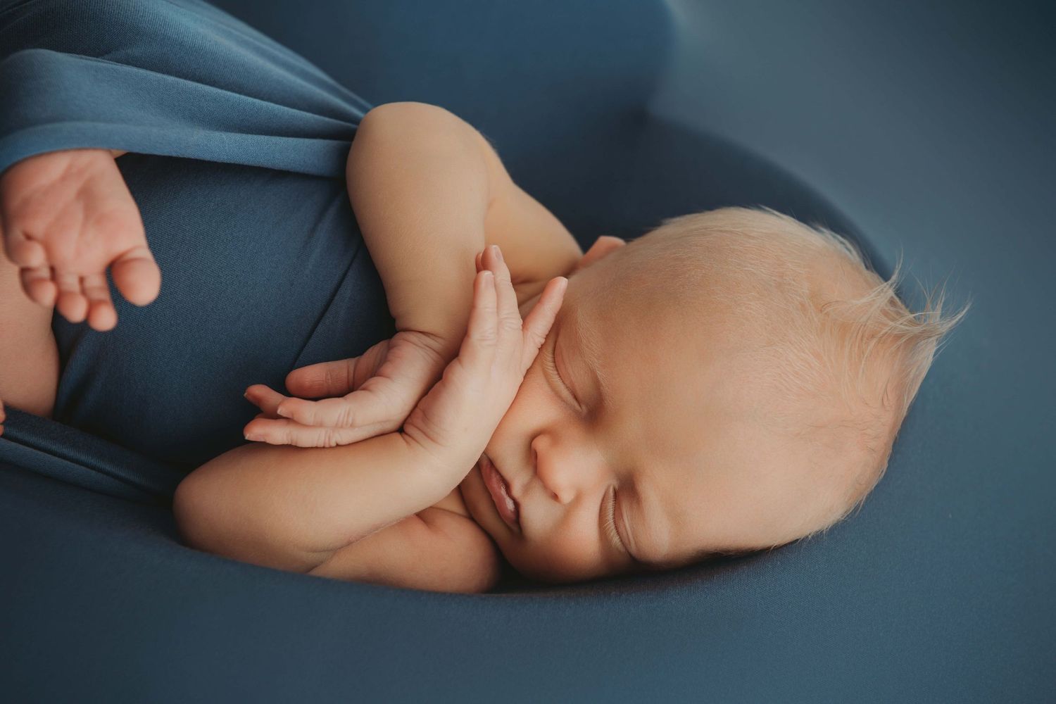 A sleeping newborn on a vibrant blue backdrop with his hands near his face and a heart shape outline.