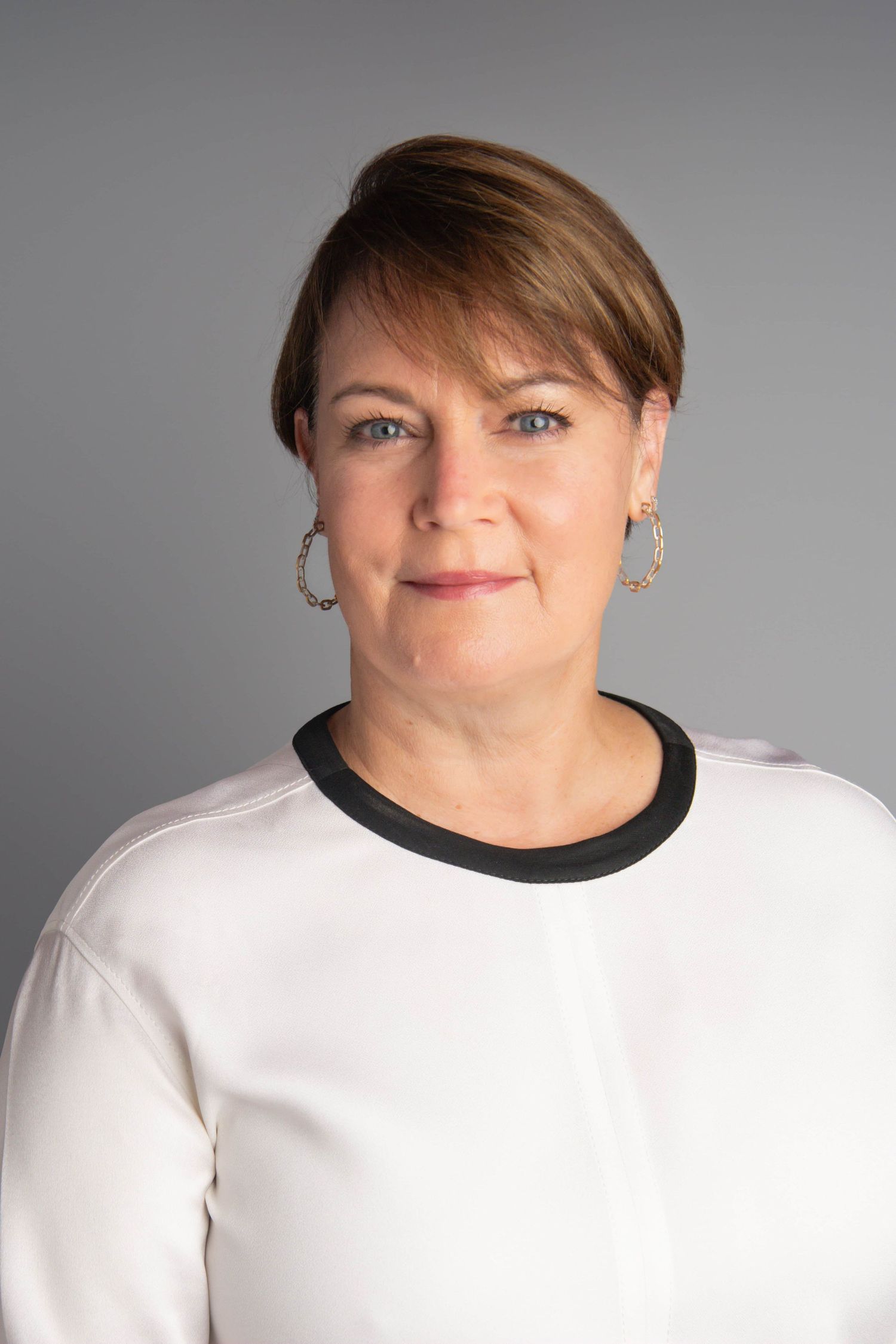 Timeless headshot of a woman wearing a white shirt and earrings on a gray backdrop.