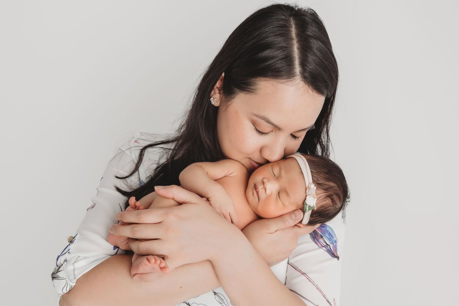 A mother holding her newborn baby and giving her a kiss as she sleeps.