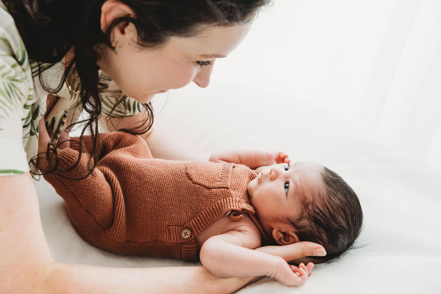 A new mother looking down at her newborn baby boy, dressed in a rust colored romper.