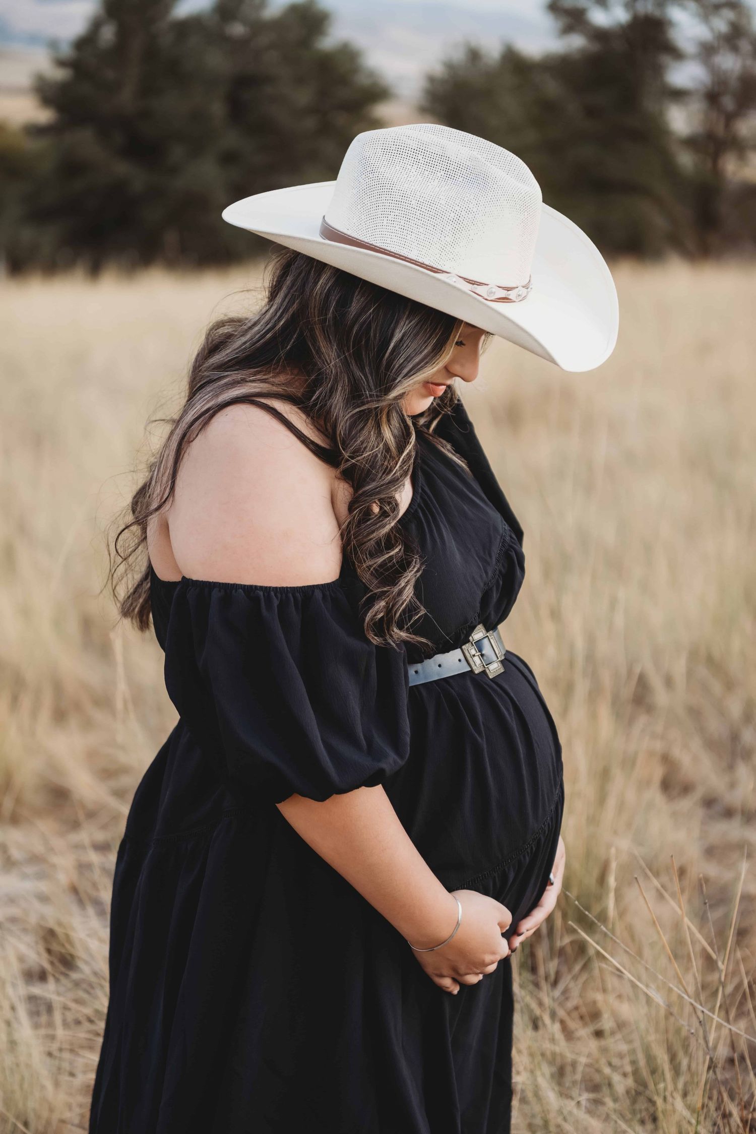 A pregnant woman wearing a white cowboy hat looking down at her pregnant belly in Walla Walla, Washington.