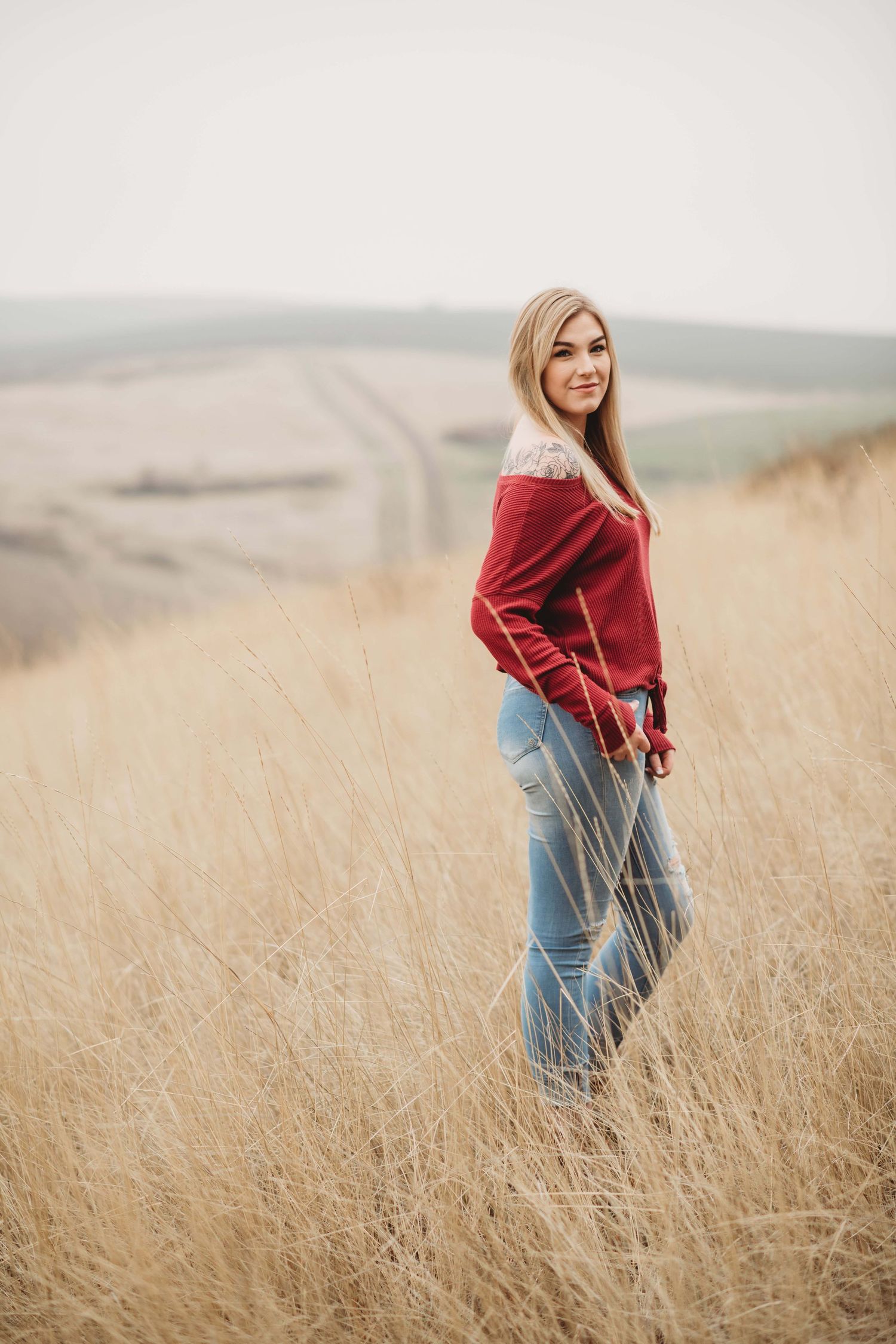 A senior portrait of a girl standing in a field with hills in the background and a path leading up the hills.