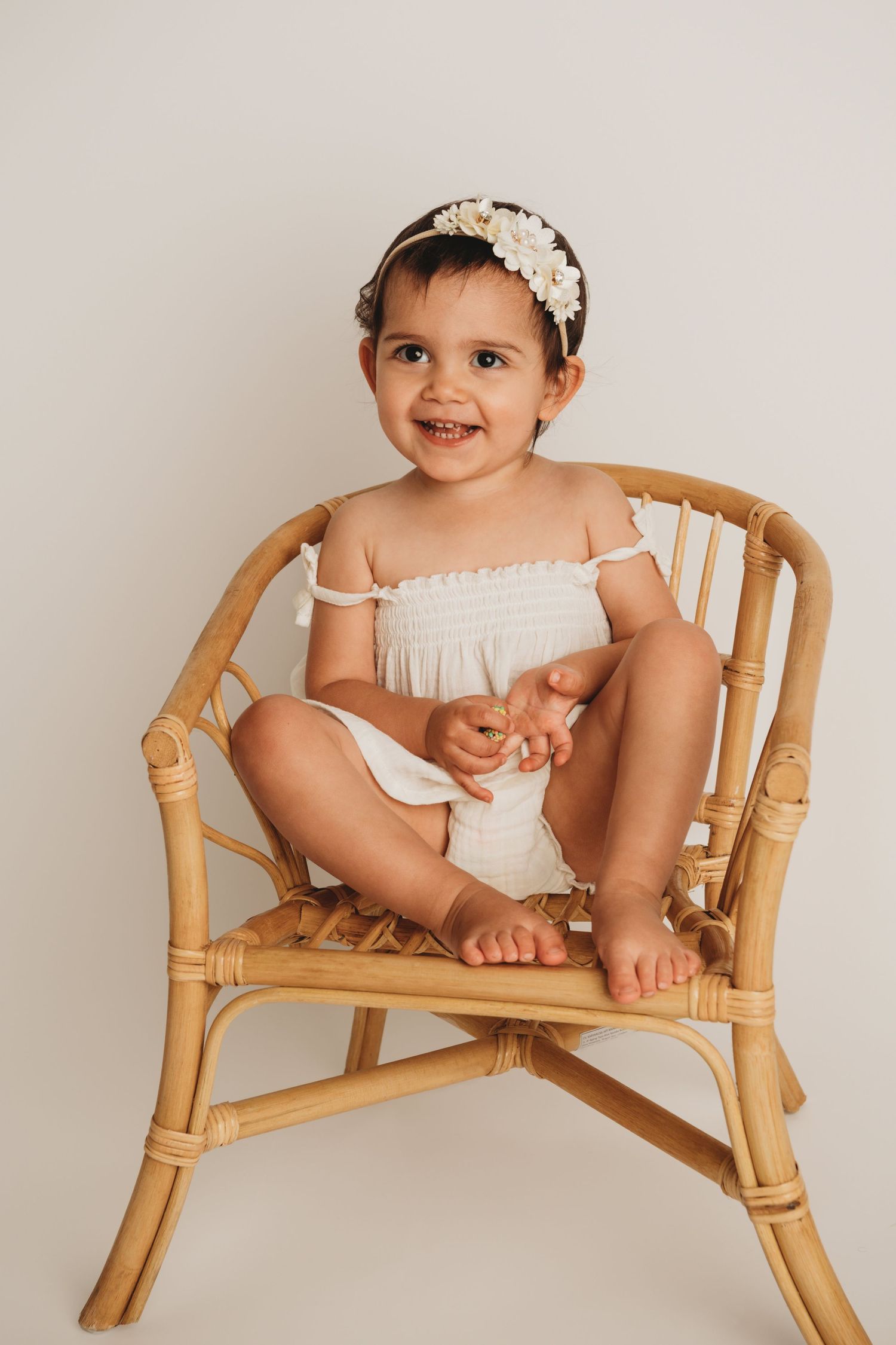 A two year old girl wearing a white floral headband sitting on a brown chair