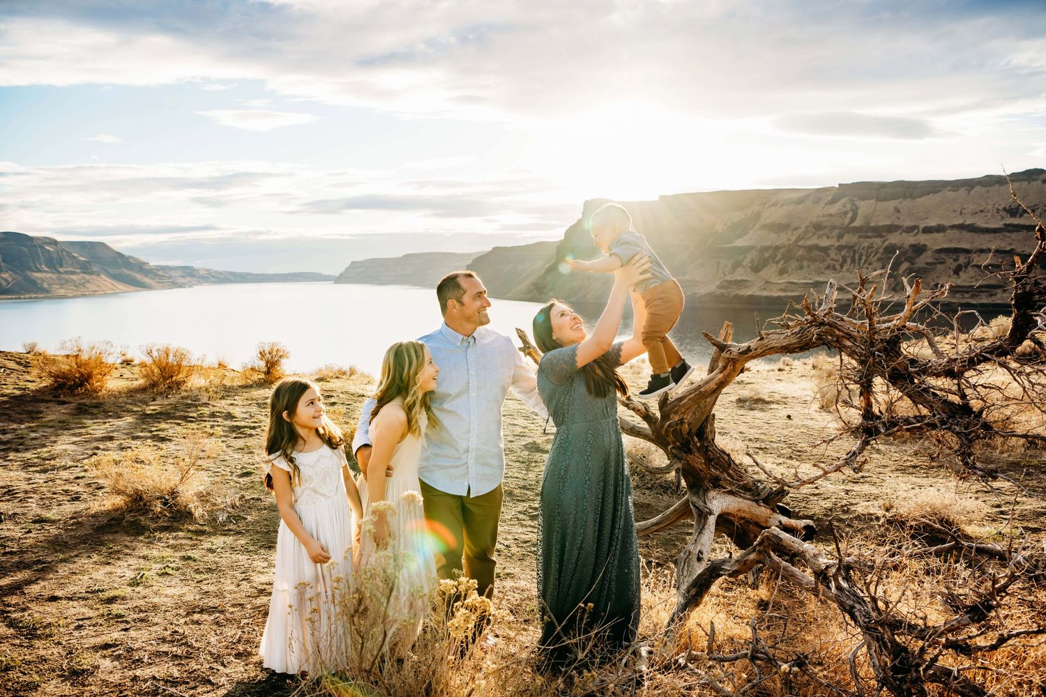 A candid moment captured of a family of five holding their baby in the air and laughing with him.