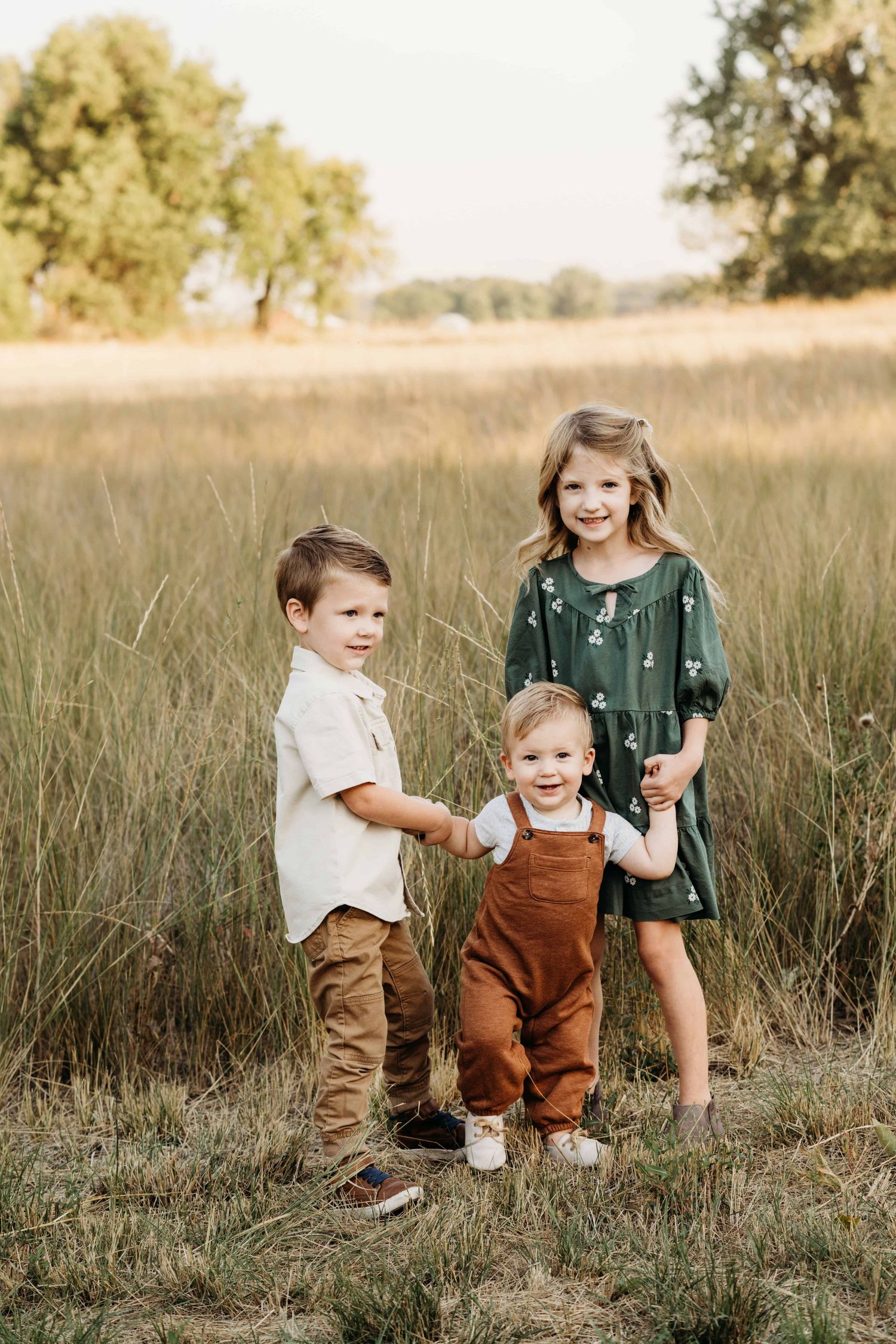Three children standing in front of a large field holding hands.