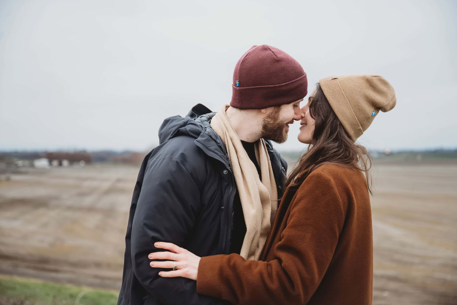 A candid picture of a couple embracing with an open field in the background.