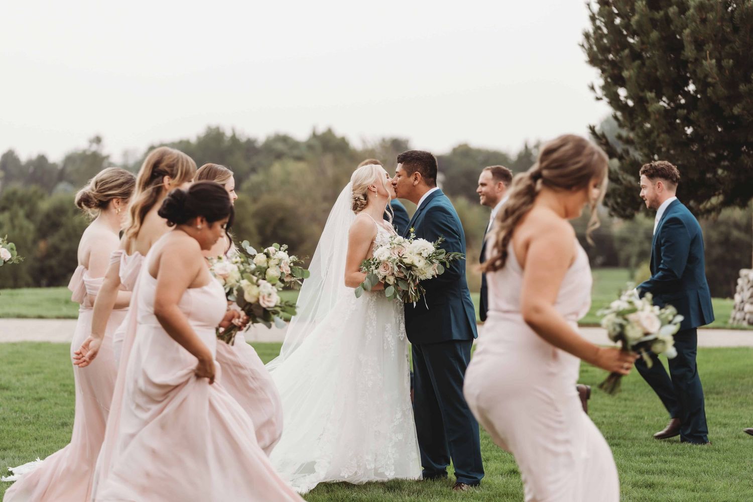 A bride and groom sharing a kiss as their wedding party walks back and forth around them.