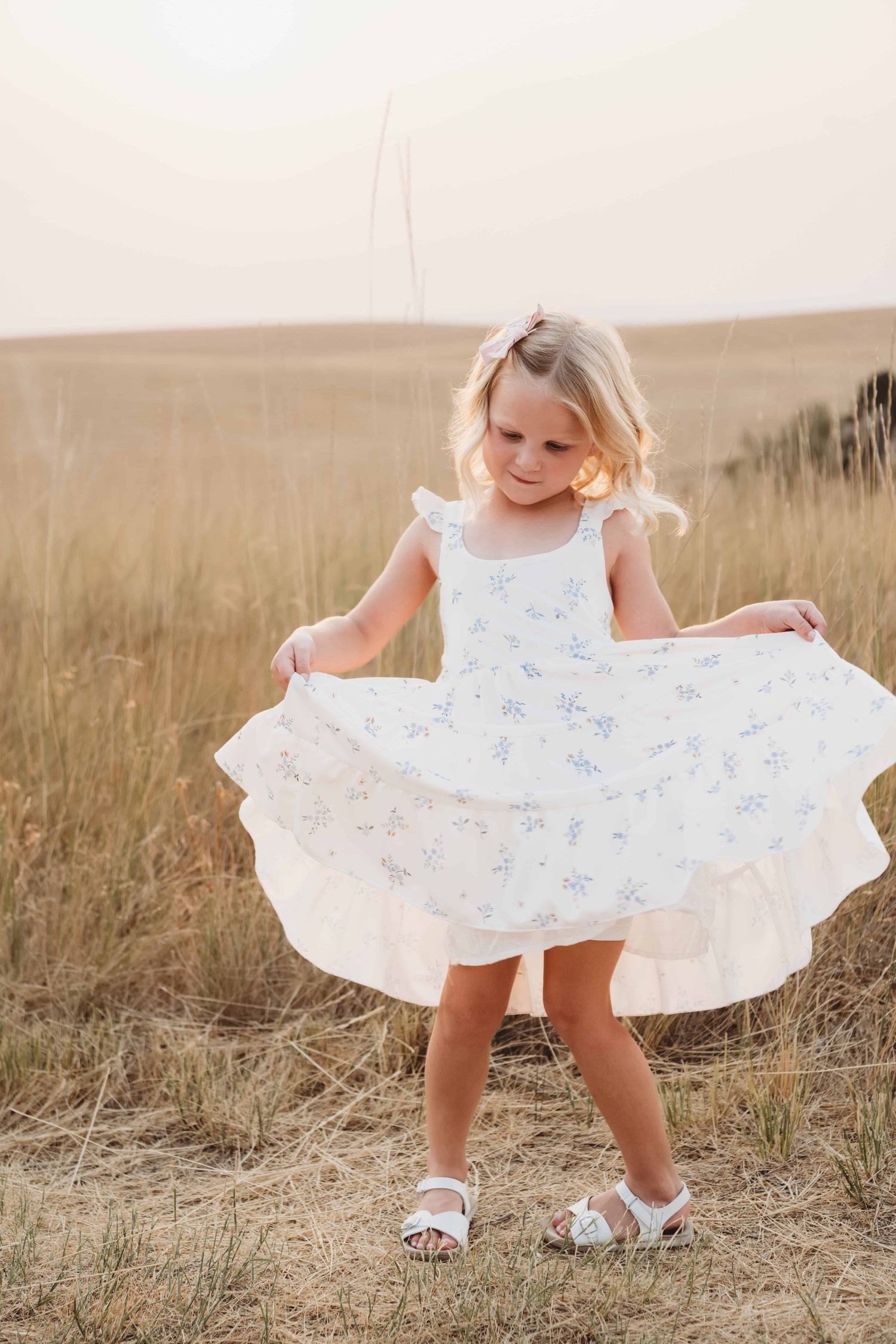 A girl holds her dress and spins in soft golden hour lighting.
