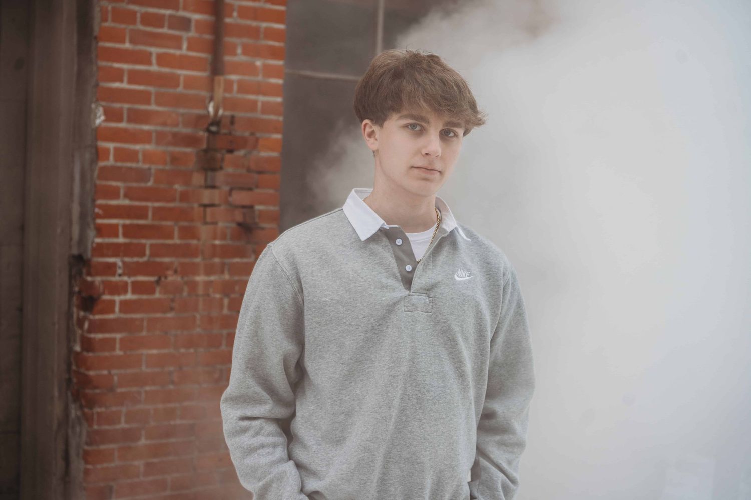 A portrait by a Walla Walla photographer of a senior standing and looking at the camera with smoke and brick walls in the background.