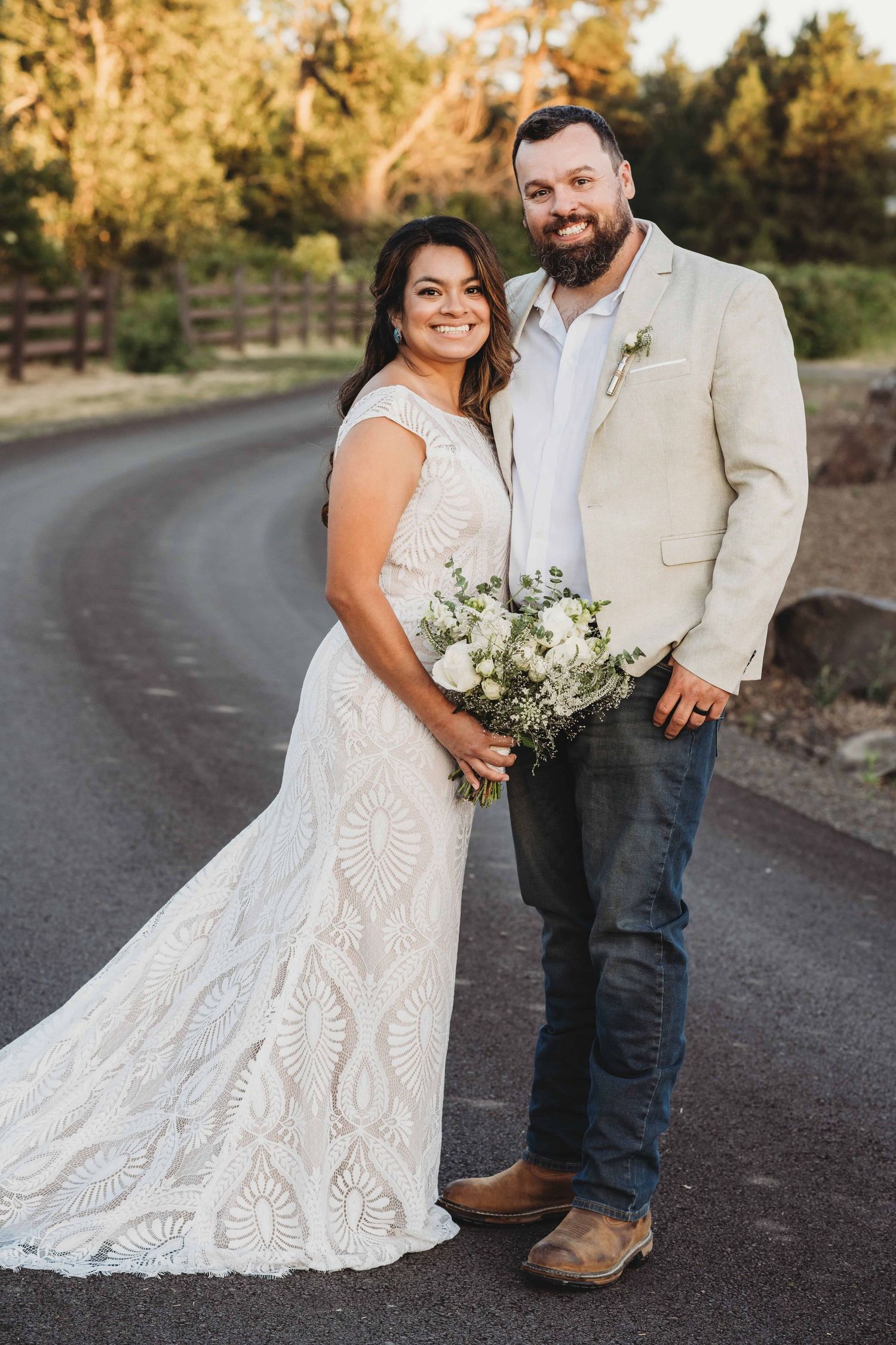 A bride and groom standing in the middle of a curvy road and smiling for the camera.