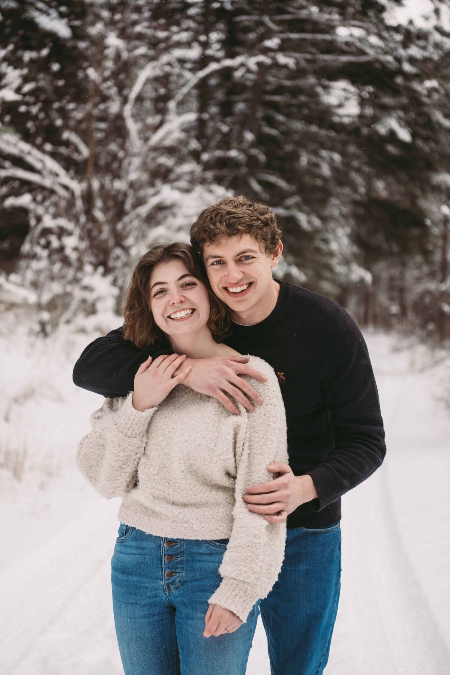 A couple hugging in the snow and smiling at the camera.