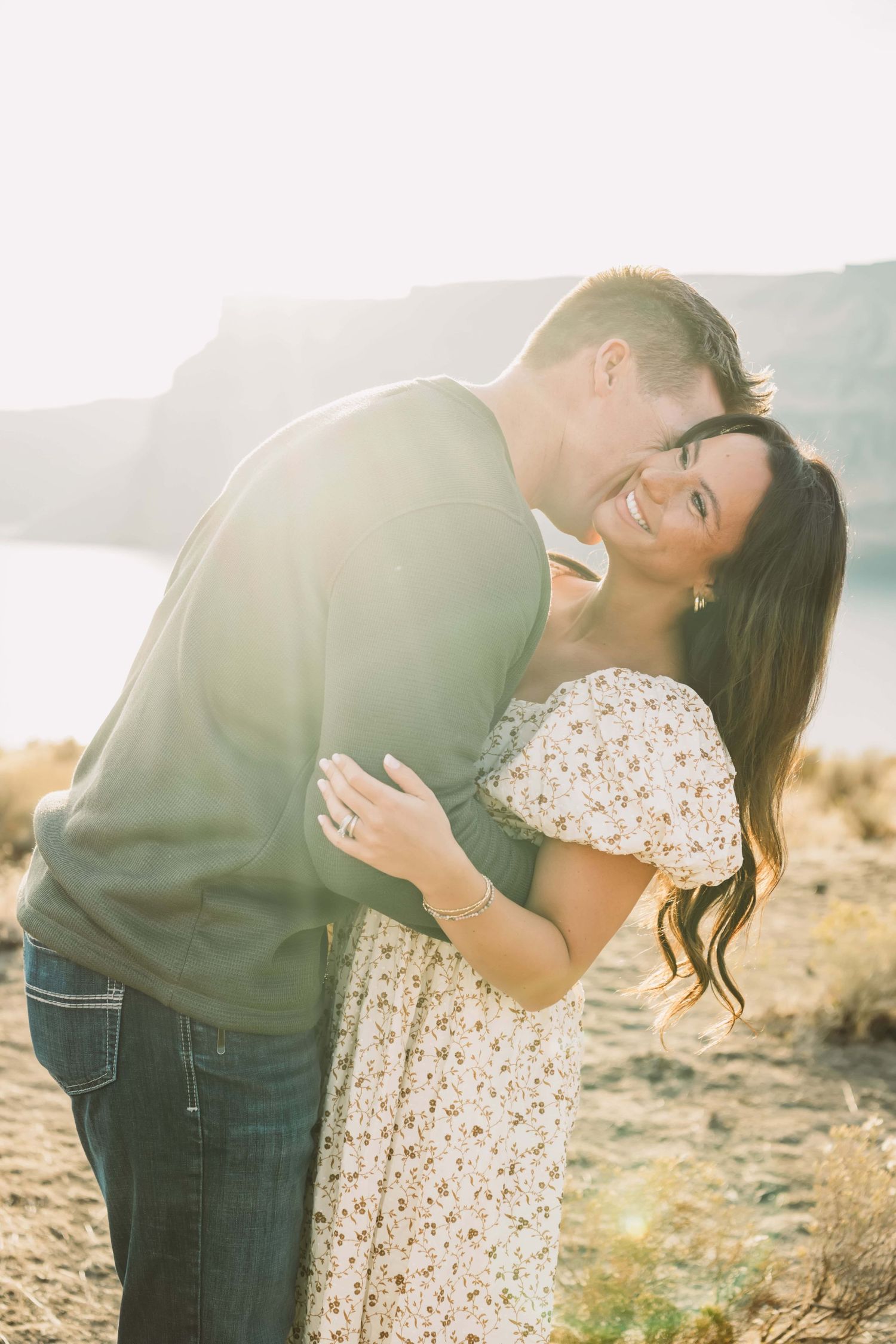 A man playfully kissing his wife with the golden sunlight shining on them.