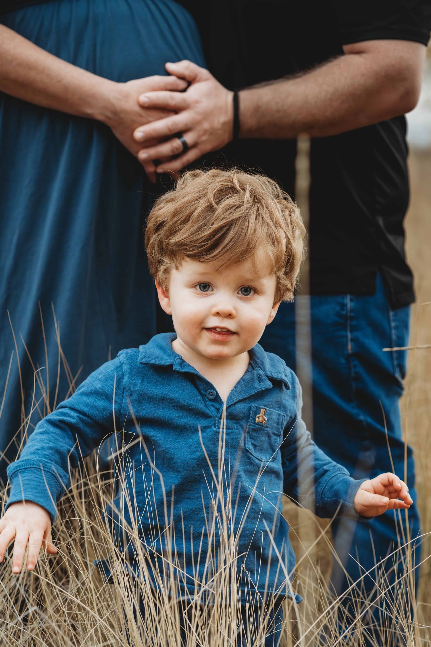 Family maternity photography in Walla Walla showing a toddler looking at the camera with parents’ hands resting on a pregnant belly.