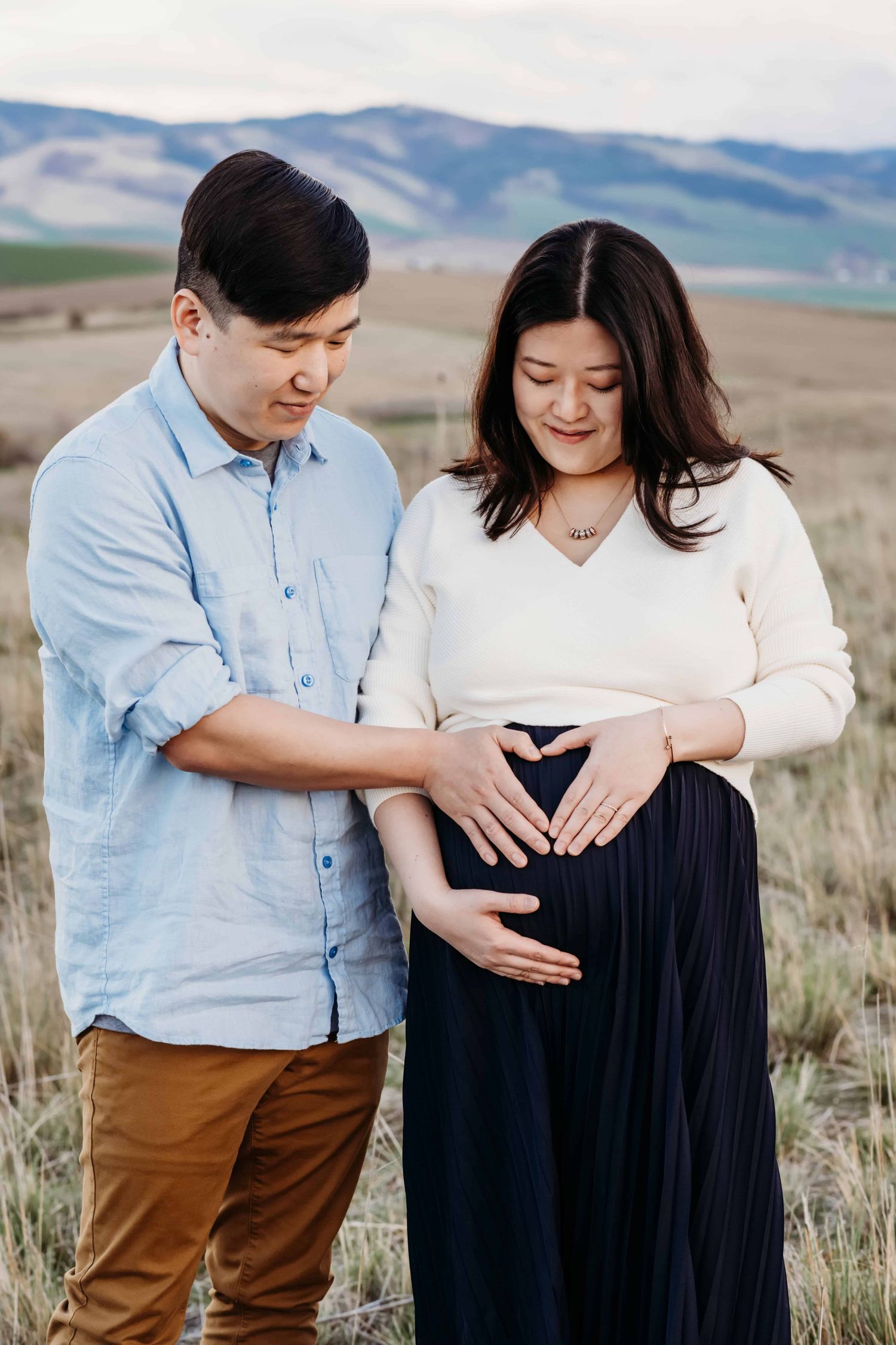 Outdoor maternity photography in Walla Walla showing a pregnant woman and her partner standing together in a field at sunset.