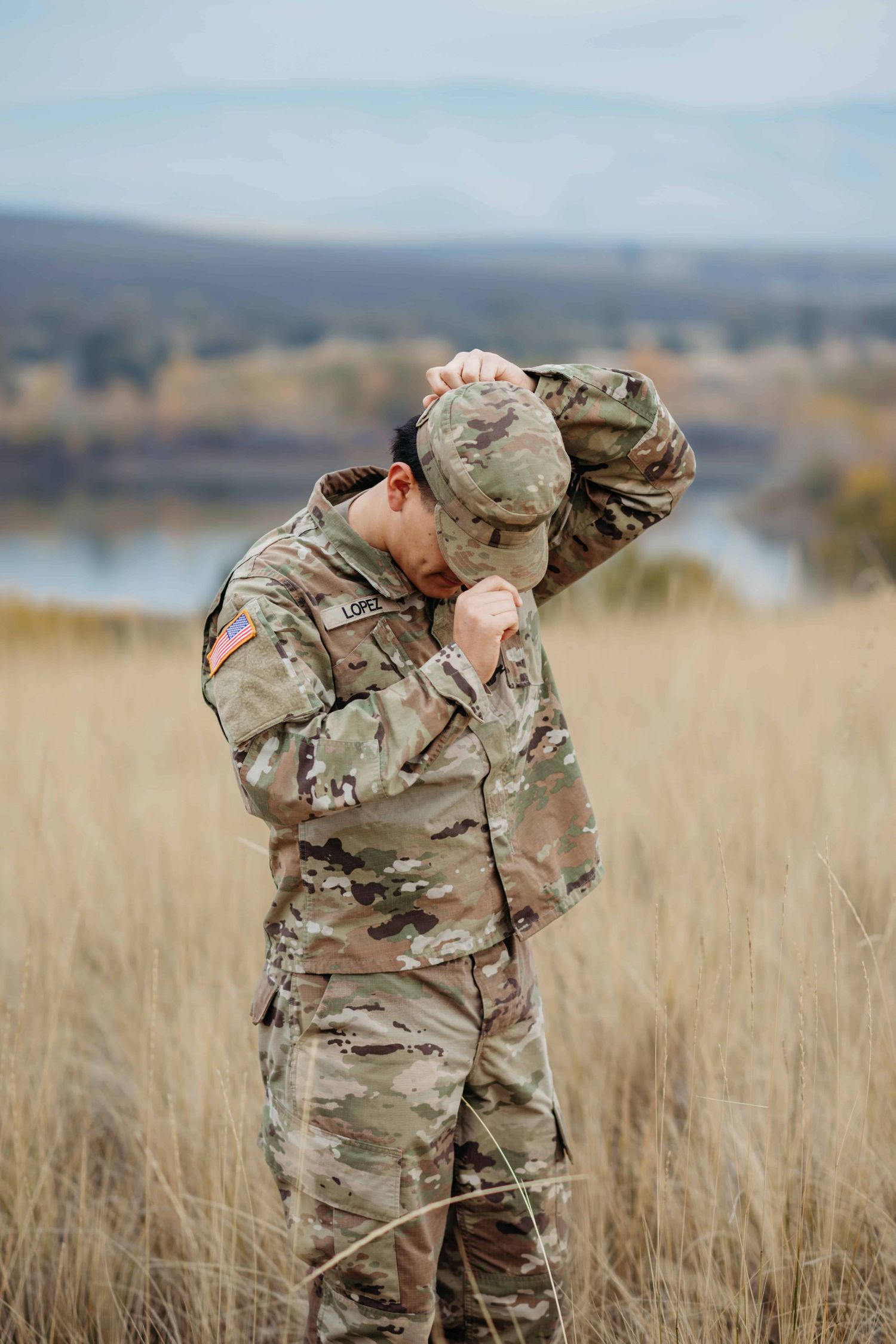 A high school senior putting on his military hat with rolling hills and a lake in the background at Bennington Lake in Walla Walla.