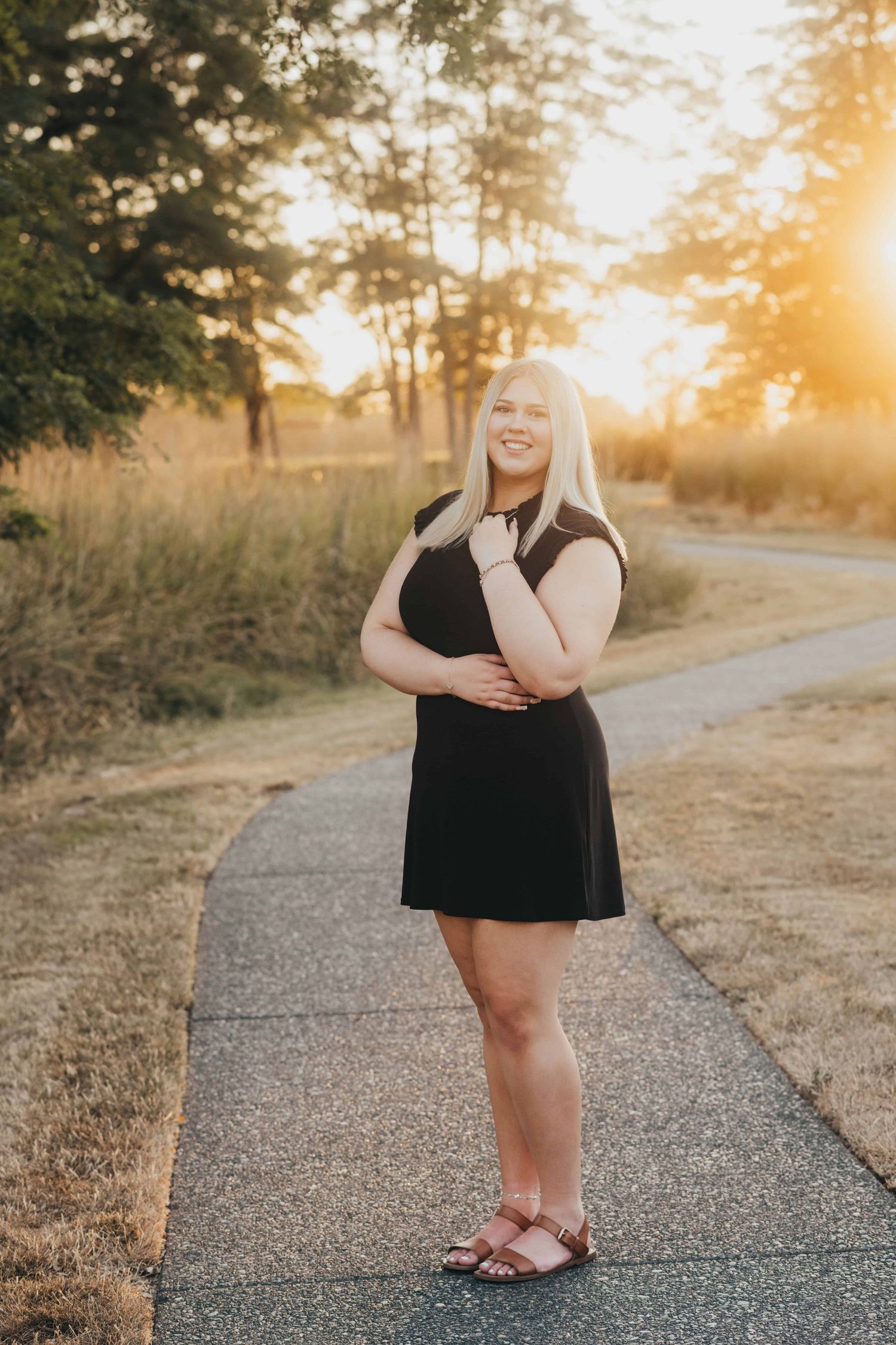 A senior wearing a black dress posing with her arms crossed and smiling at the camera, taken by a Walla Walla senior photographer.