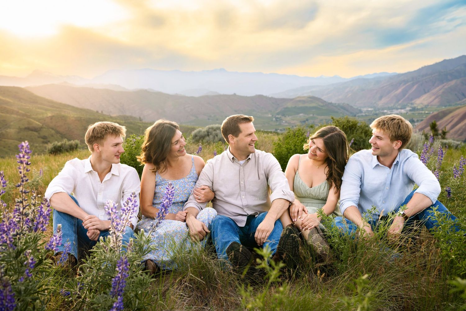 A family sitting together and looking in at each other surrounded by wildflowers and mountains, taken by a Wenatchee family photographer.