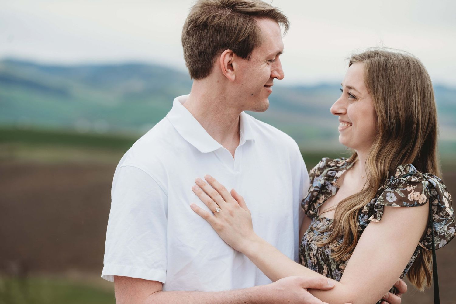 A couple embracing and smiling with rolling hills behind them.